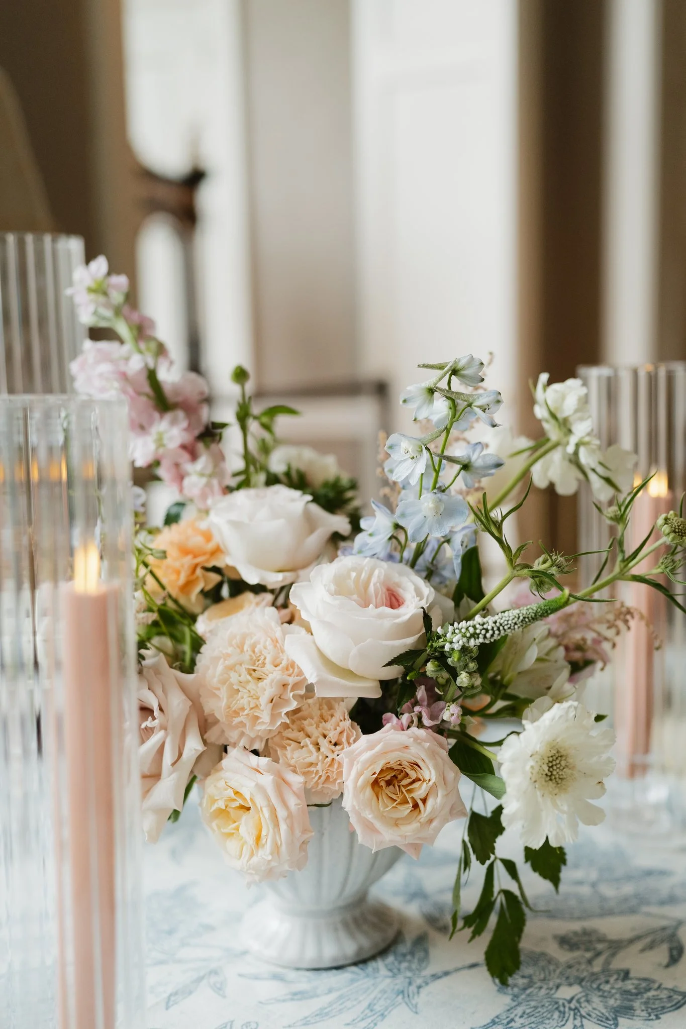 A floral arrangement of white, pink, and light peach flowers in a white ceramic vase on a table with a blue and white patterned tablecloth in Memphis, TN. 