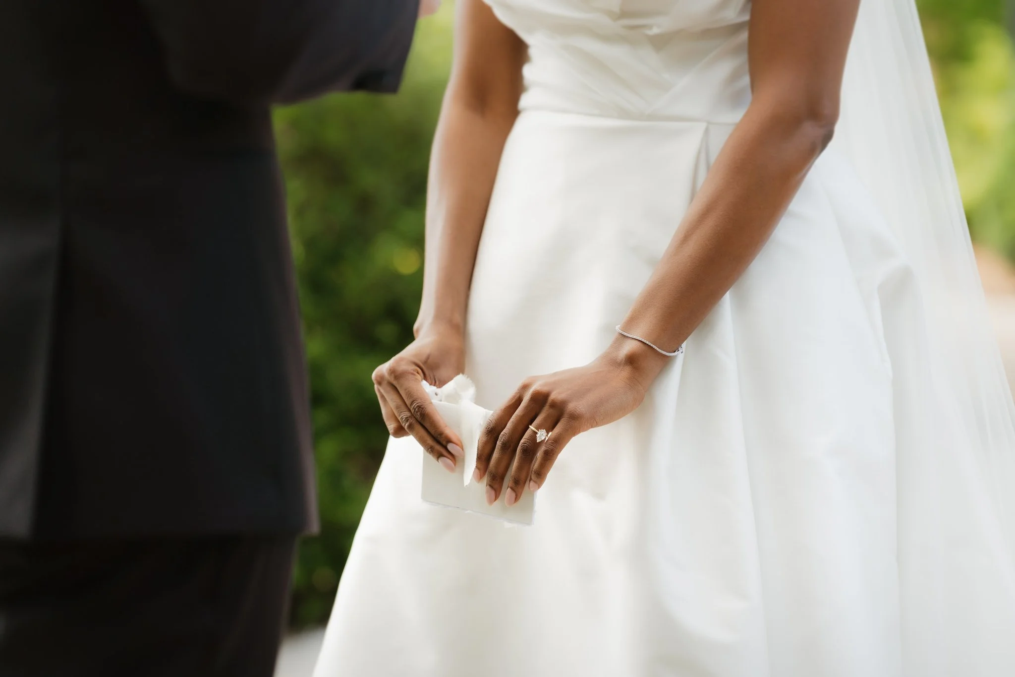 Close-up of a bride and groom holding hands during their wedding ceremony outdoors, with the bride wearing a white dress and a ring visible on her finger in Memphis, TN. 