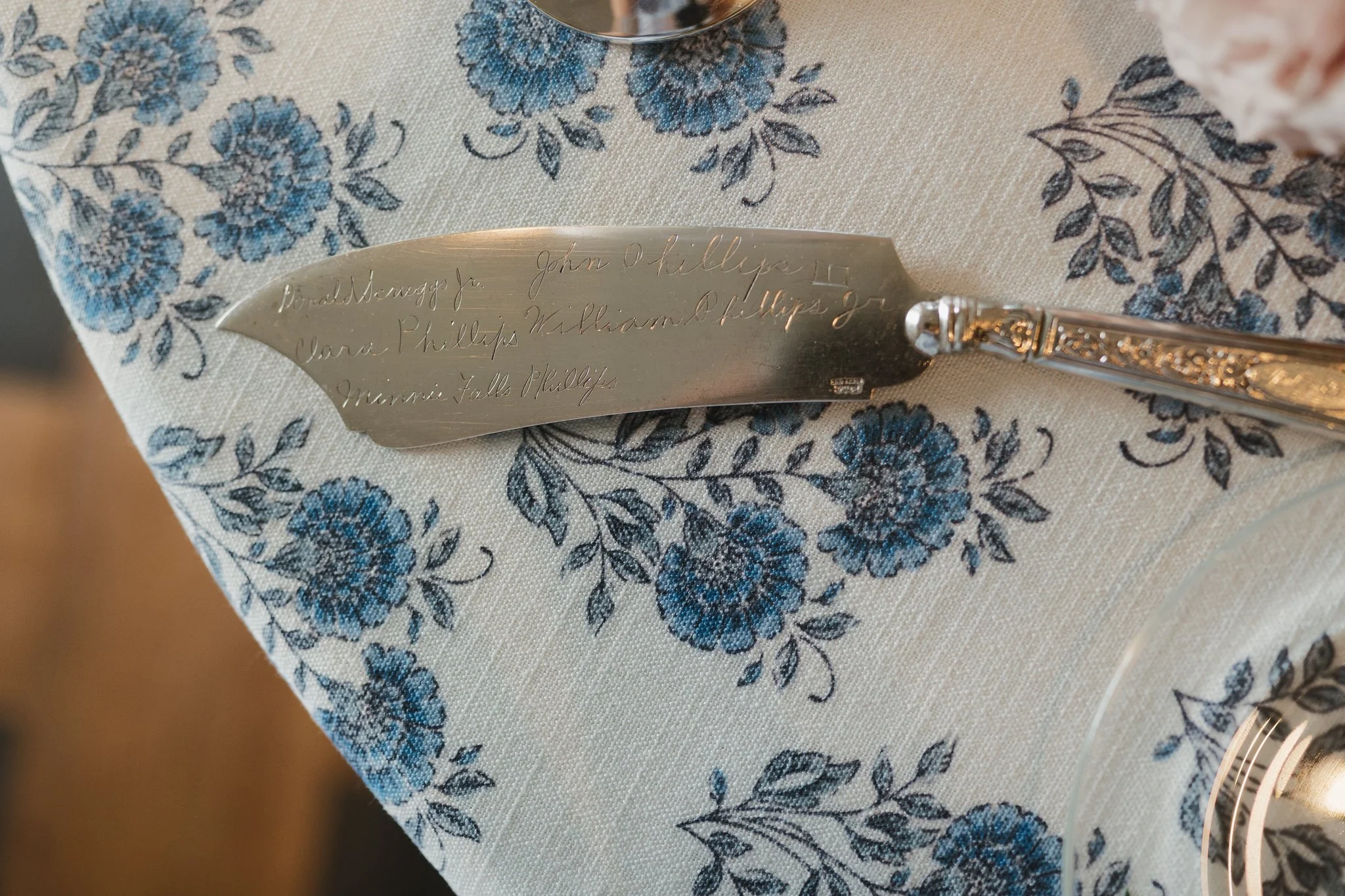 Close-up of engraved silverware with names, placed on a blue floral tablecloth in Memphis, TN. 