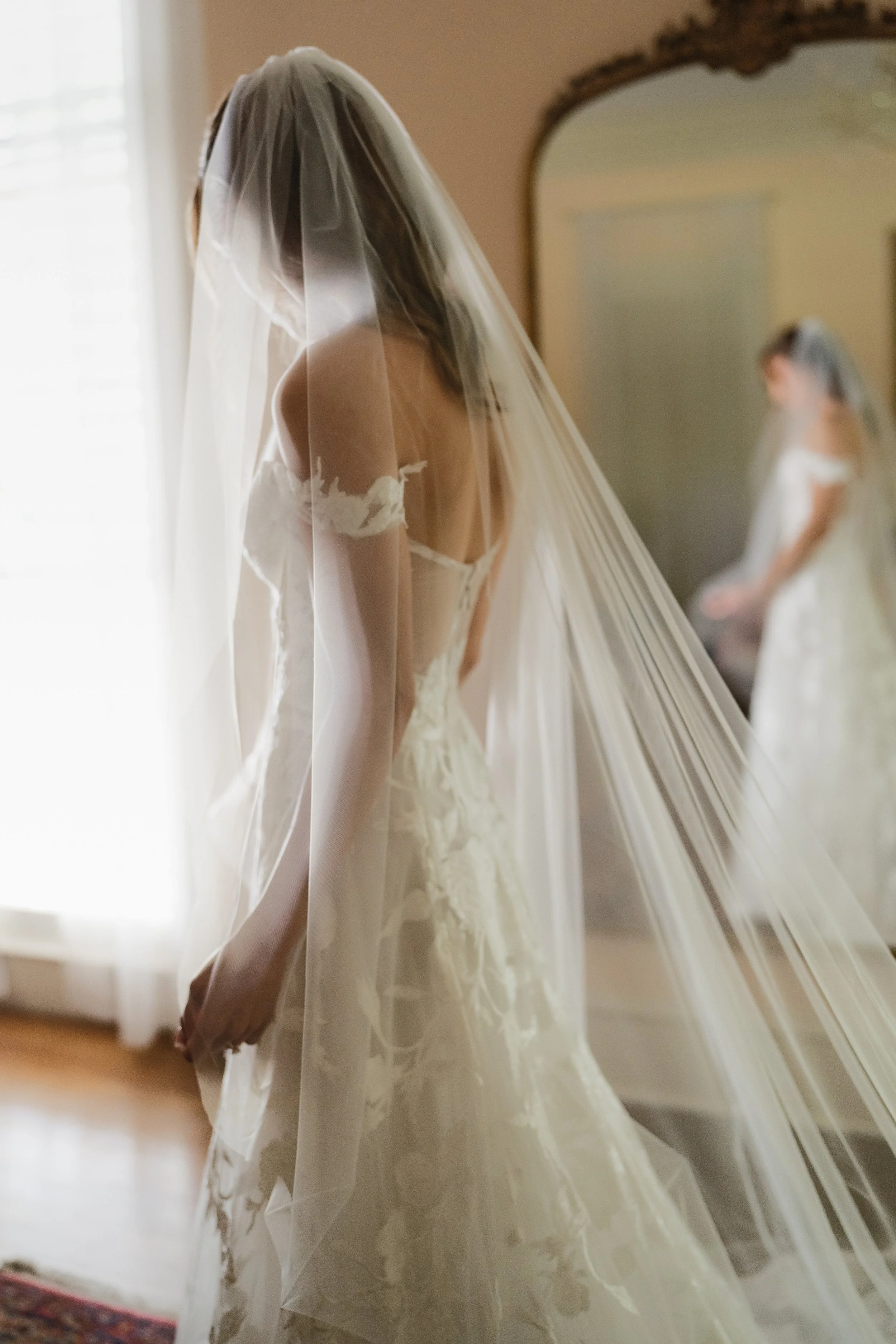 A bride standing in front of a mirror wearing a wedding dress and veil, with her reflection visible in the mirror in Memphis, TN. 
