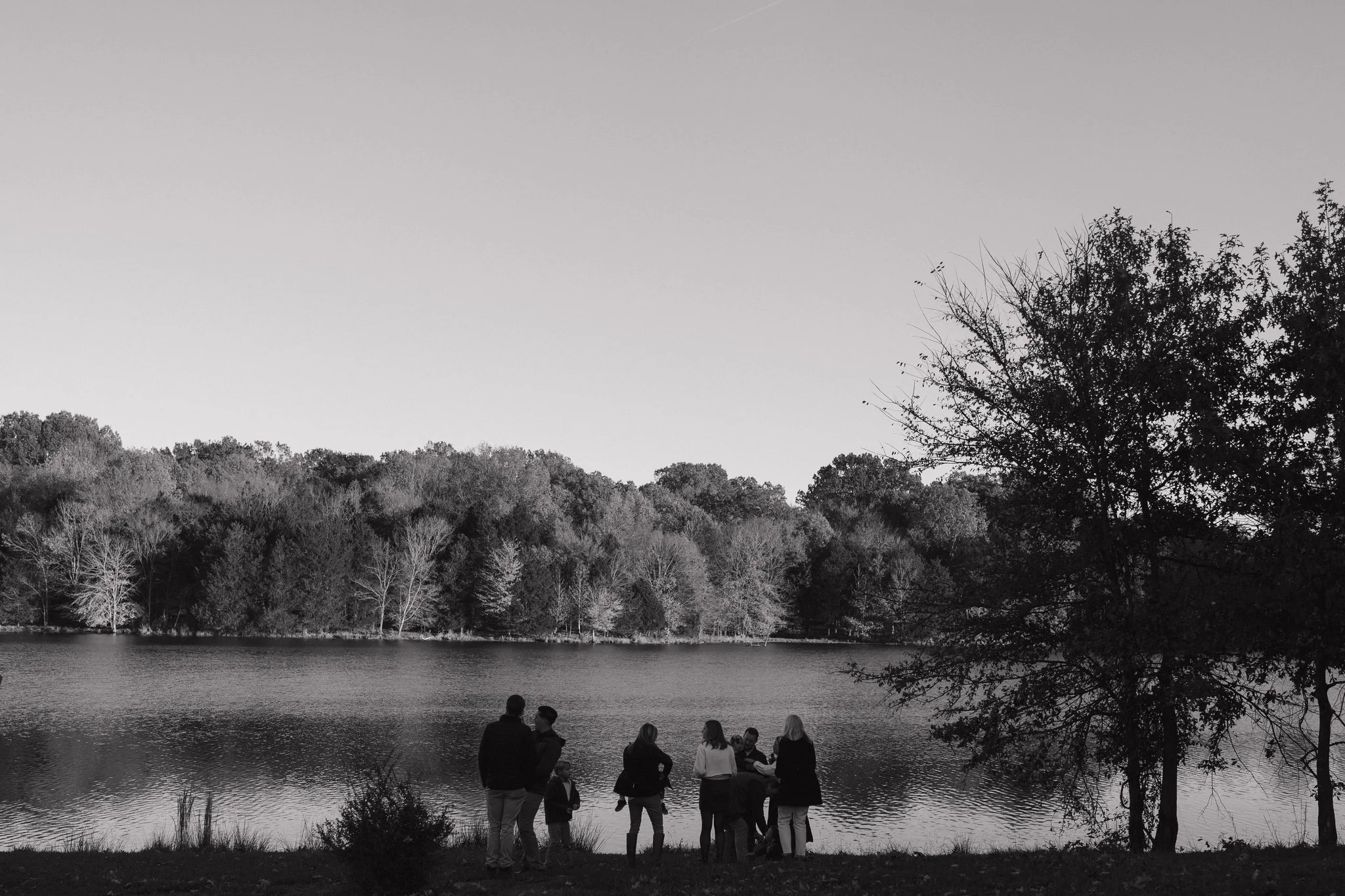 People standing by a lake at dusk, with trees and hills in the background in Memphis, TN. 