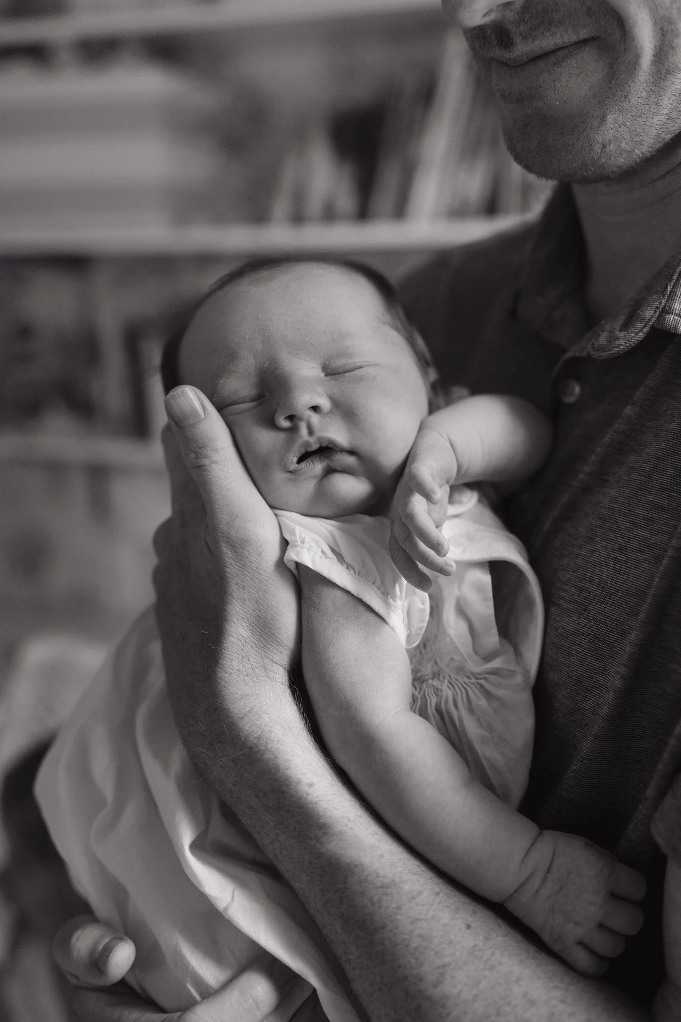 A person gently holding a sleeping baby's head and arm, with the baby's face resting against the person's chest in a caring embrace in Memphis, TN. 