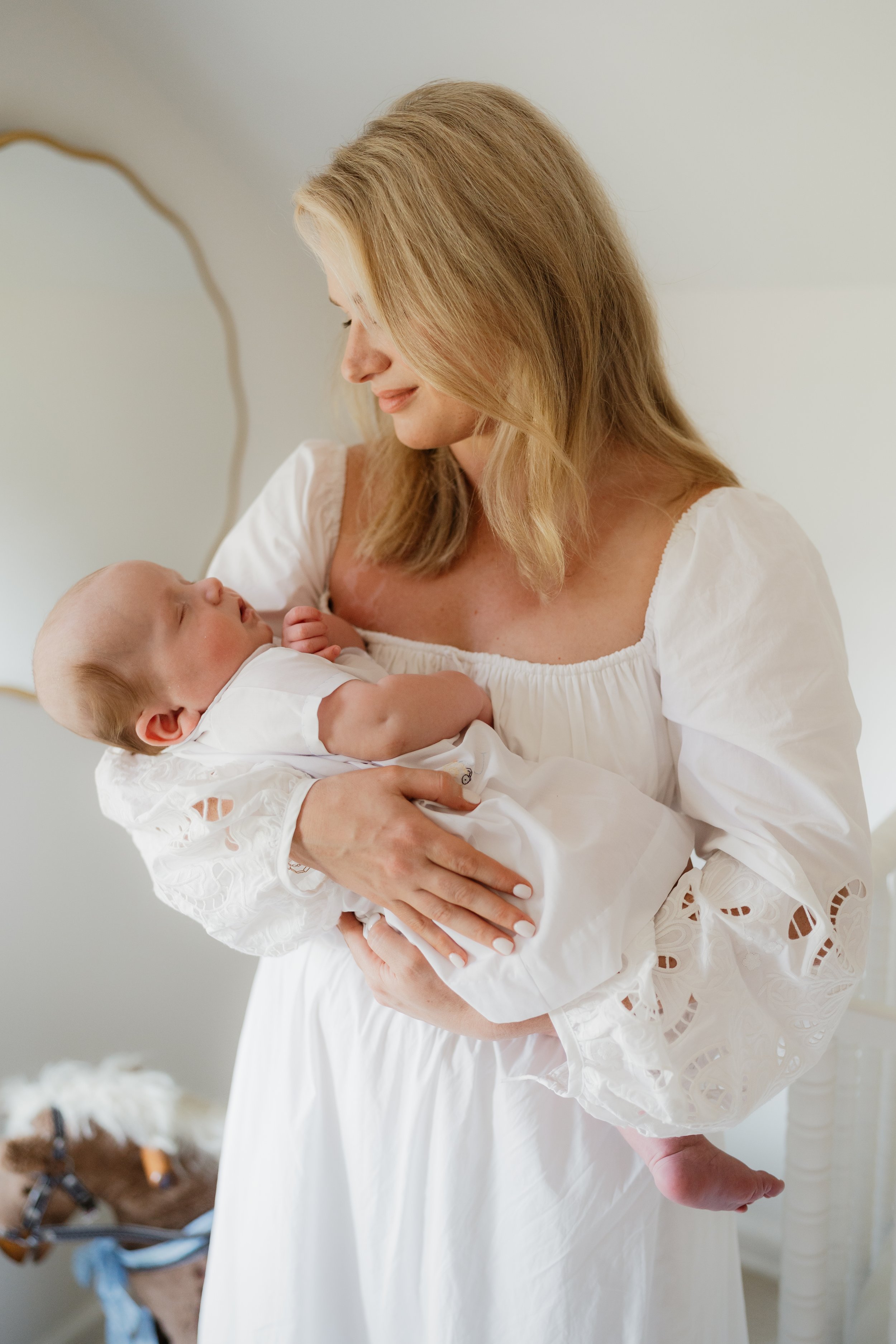 A woman in a white dress holding a sleeping baby in her arms, both dressed in white, in a softly lit room with neutral-colored background in Memphis, TN. 