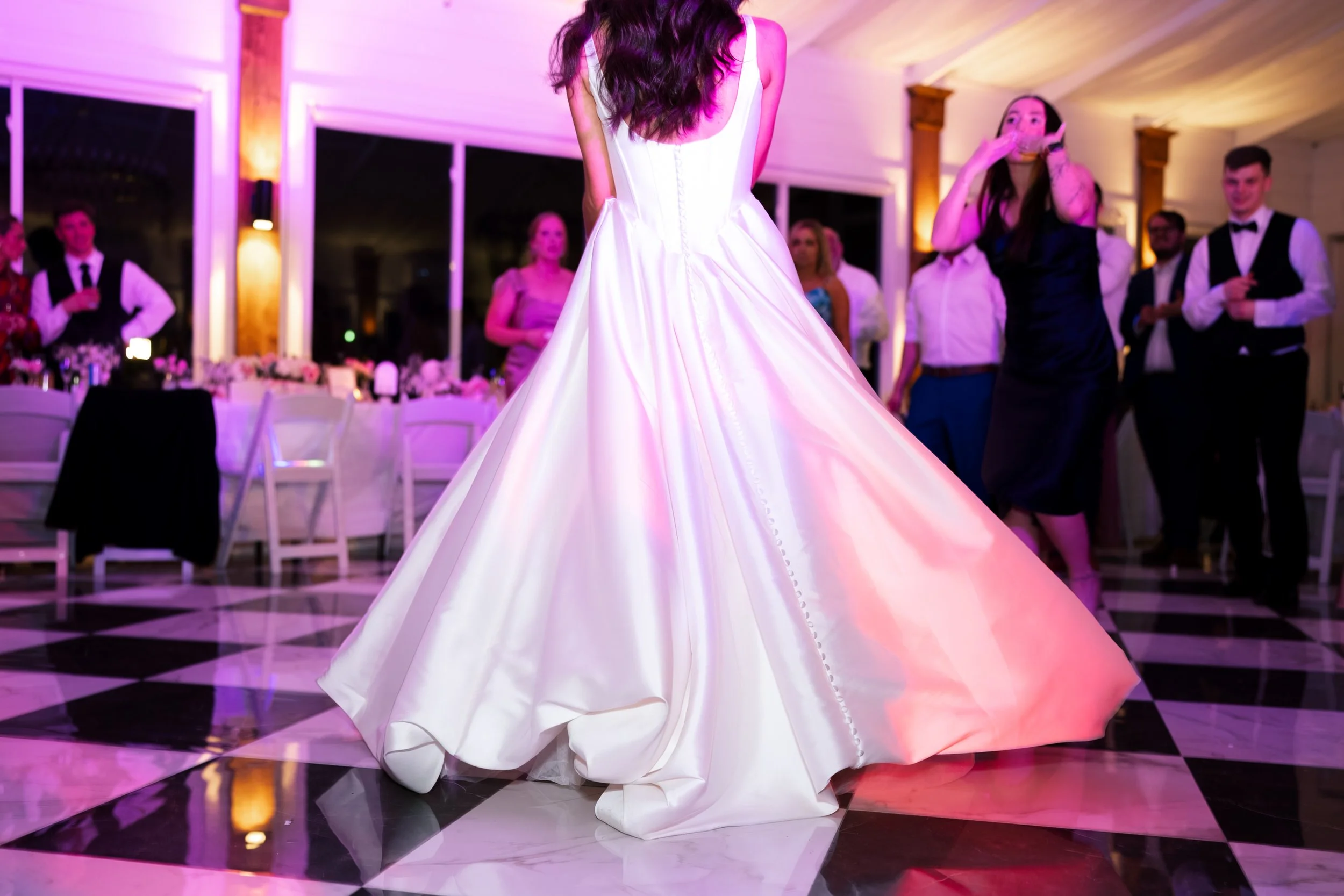 A person in a white wedding dress dancing at a reception with people watching, in a decorated venue with pink and purple lighting in Memphis, TN. 