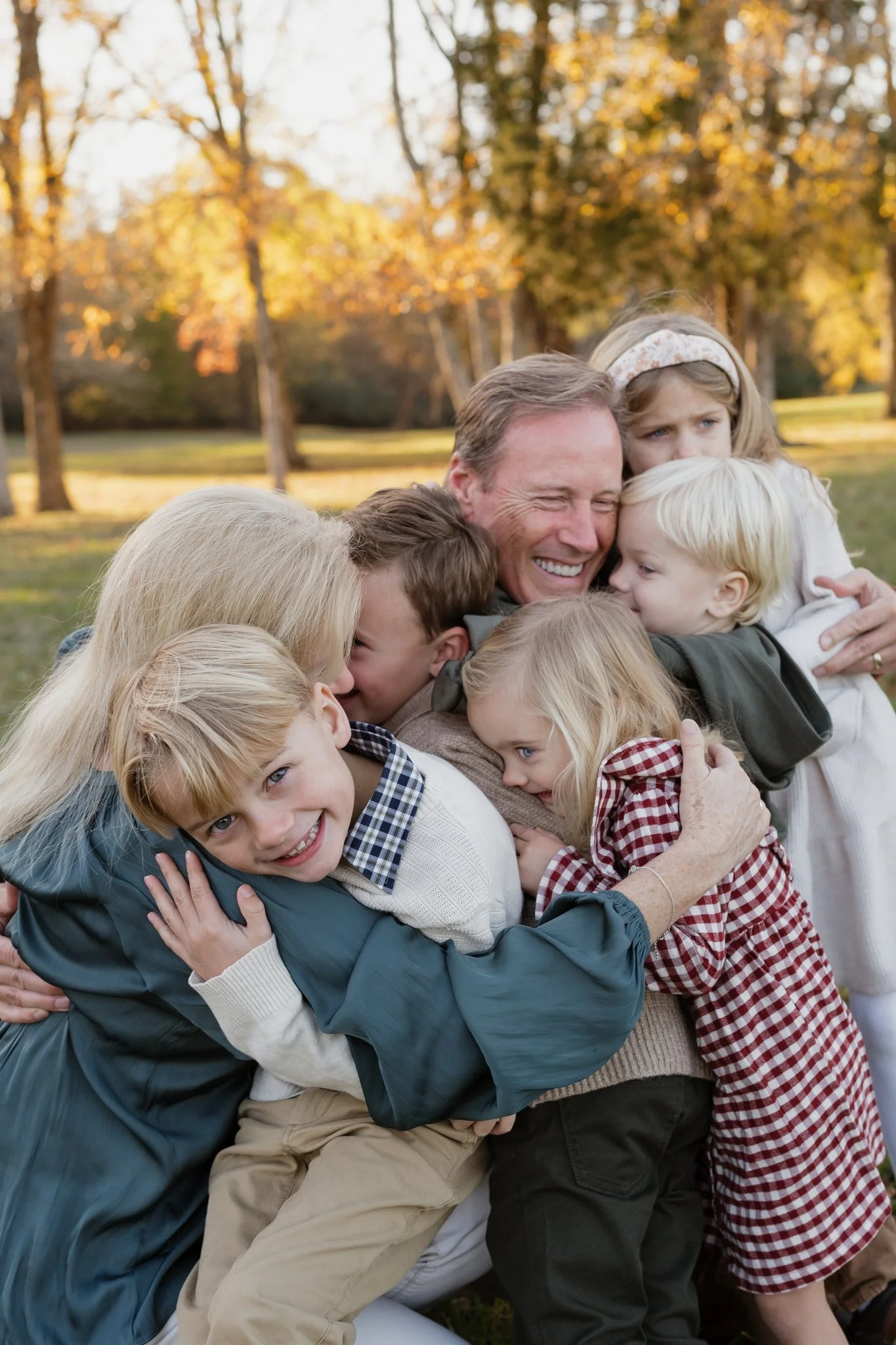 A diverse family group of adults and children of different ages and ethnicities hugging and smiling in an outdoor park with autumn trees in Memphis, TN. 