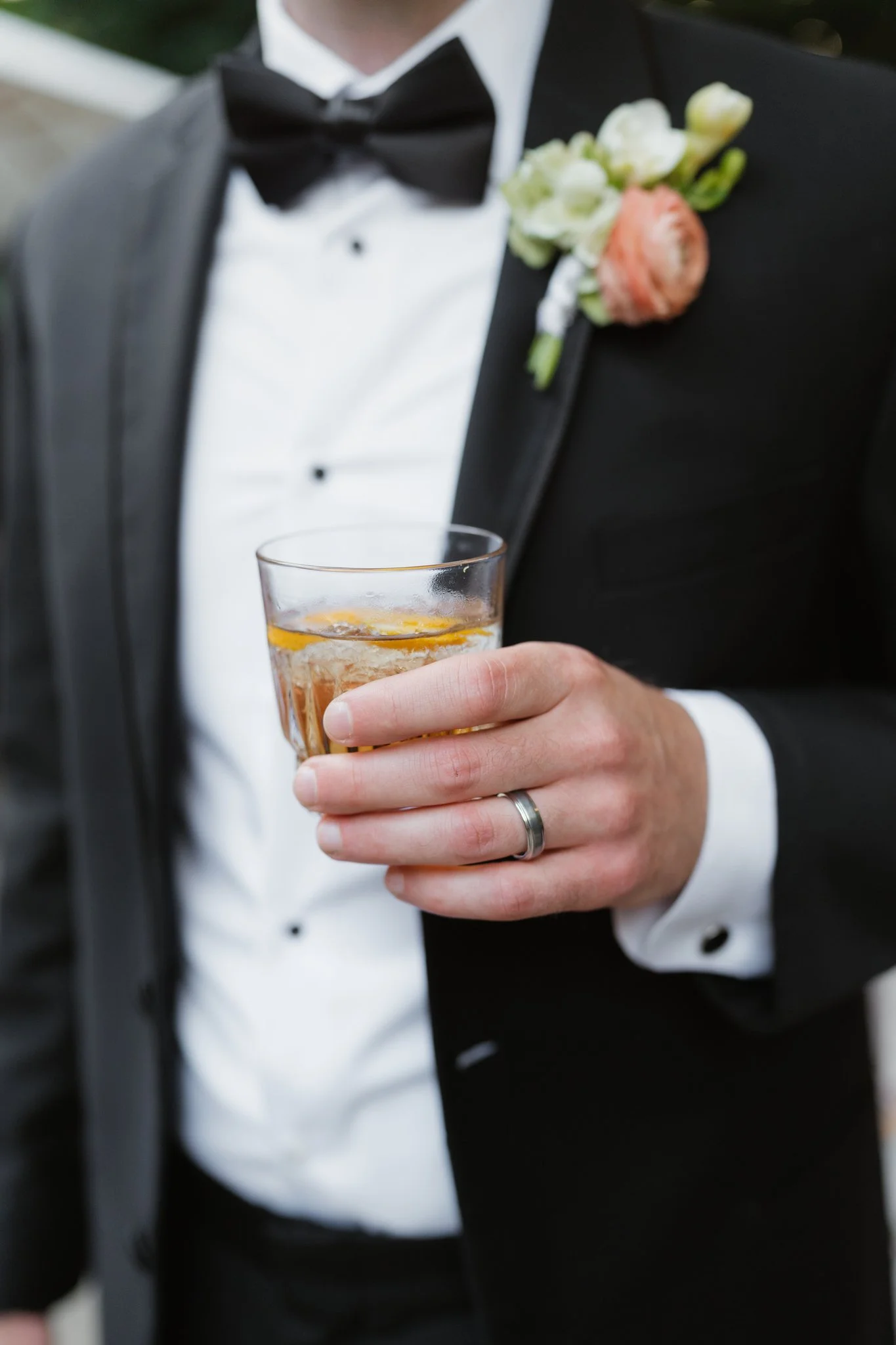 A man in a tuxedo holding a glass of beverage, with a boutonniere on his jacket lapel in Memphis, TN. 