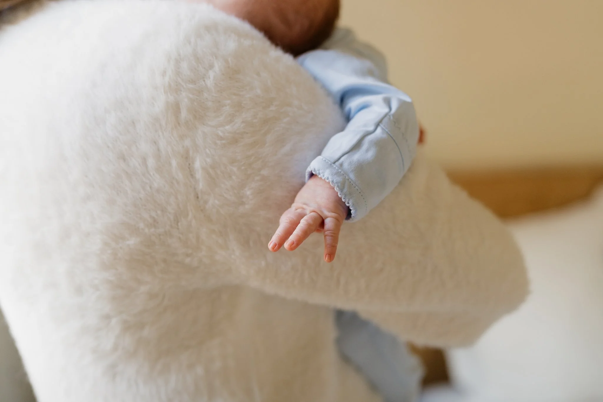 Close-up of a small child's hand hanging off the side of her mom, with a tan wall in the background in Memphis, TN. 