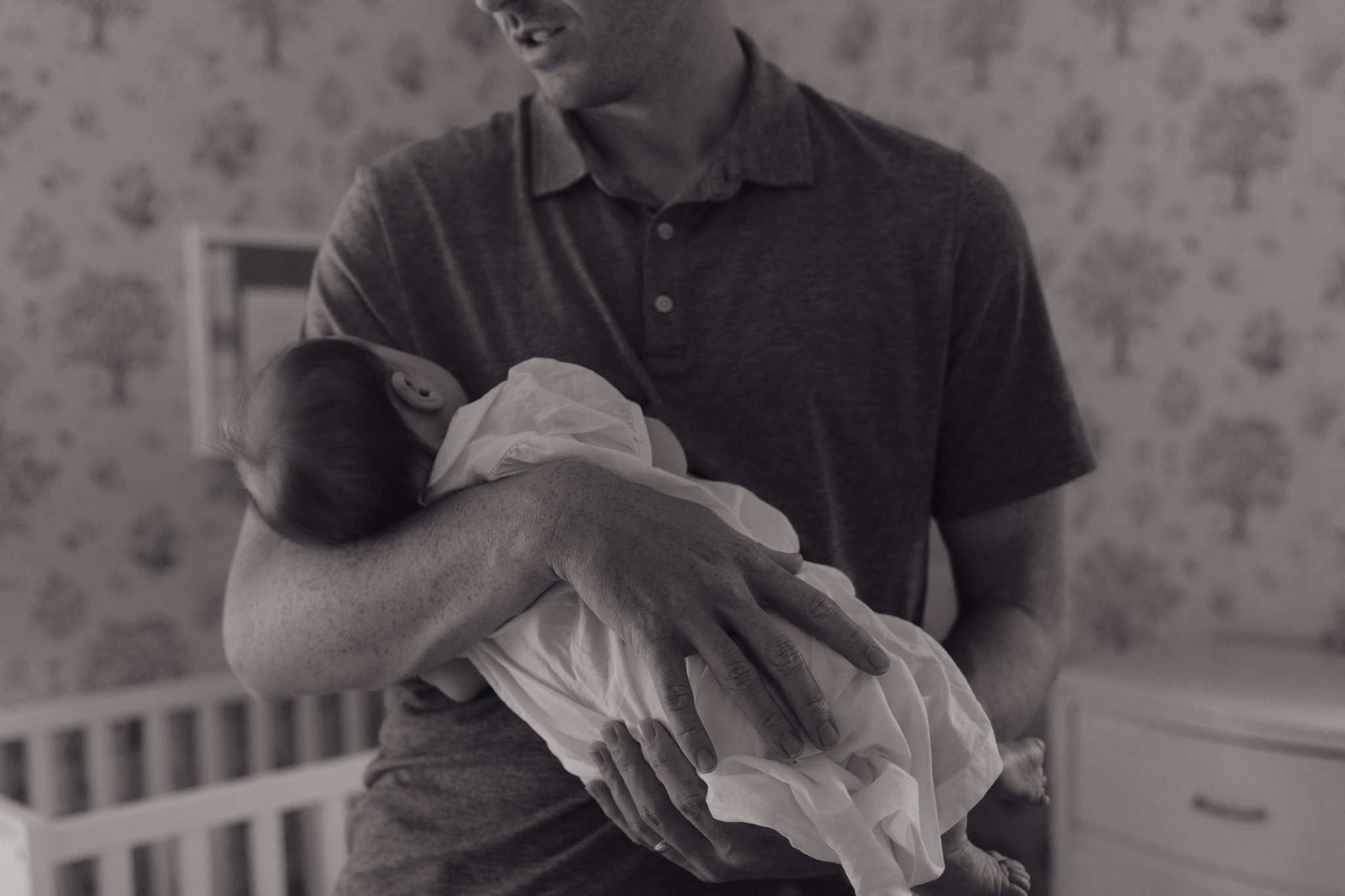 A person is holding a newborn baby in their hands, with a background of a wall decorated with small floral patterns  in Memphis, TN. 