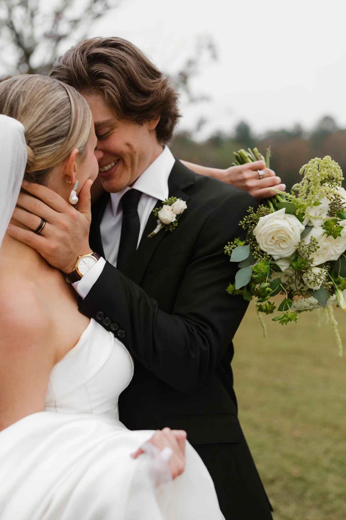 A newlywed couple sharing a kiss outdoors, the groom in a black tuxedo with a white boutonniere, and the bride in a white wedding gown, holding a bouquet of white flowers in Memphis, TN. 