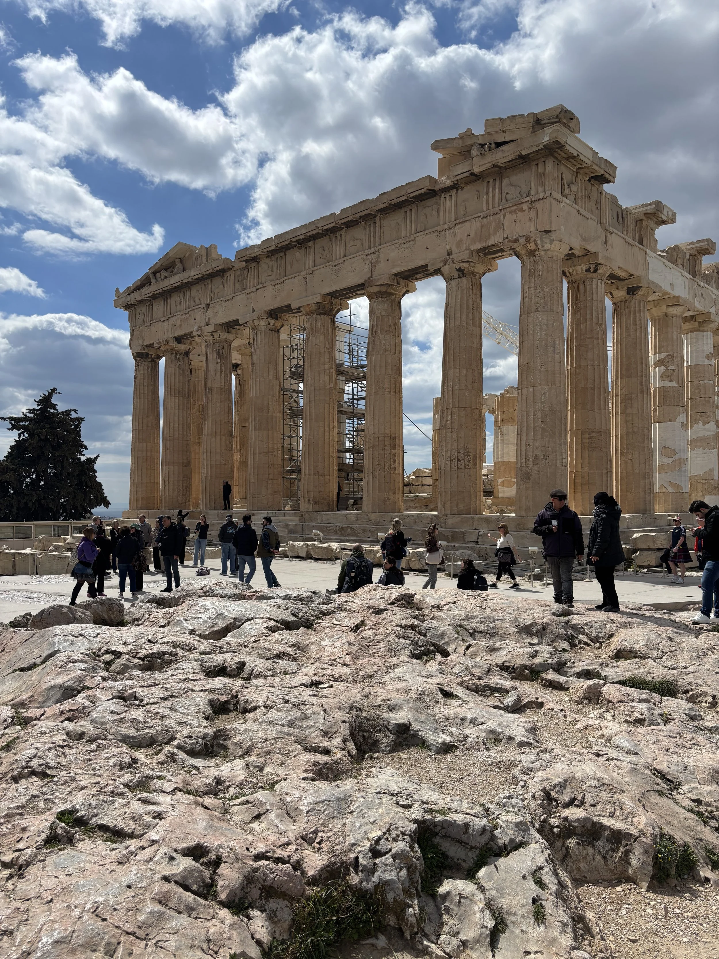 Tourists at the Parthenon temple ruins on a partly cloudy day in Athens, Greece.
