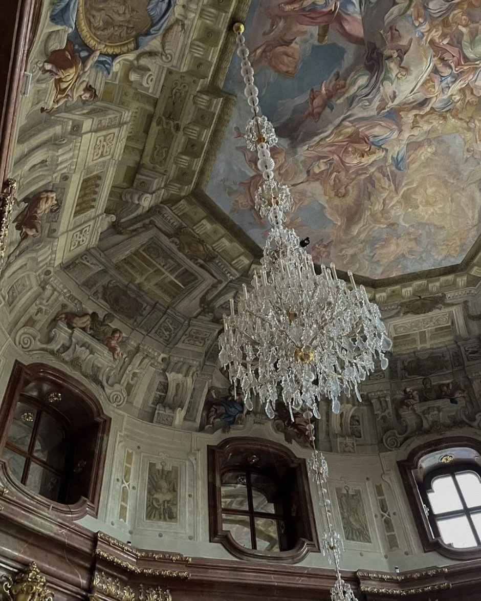 Interior of an opulent room with ornate painted ceiling, a large chandelier, and decorative architectural details.