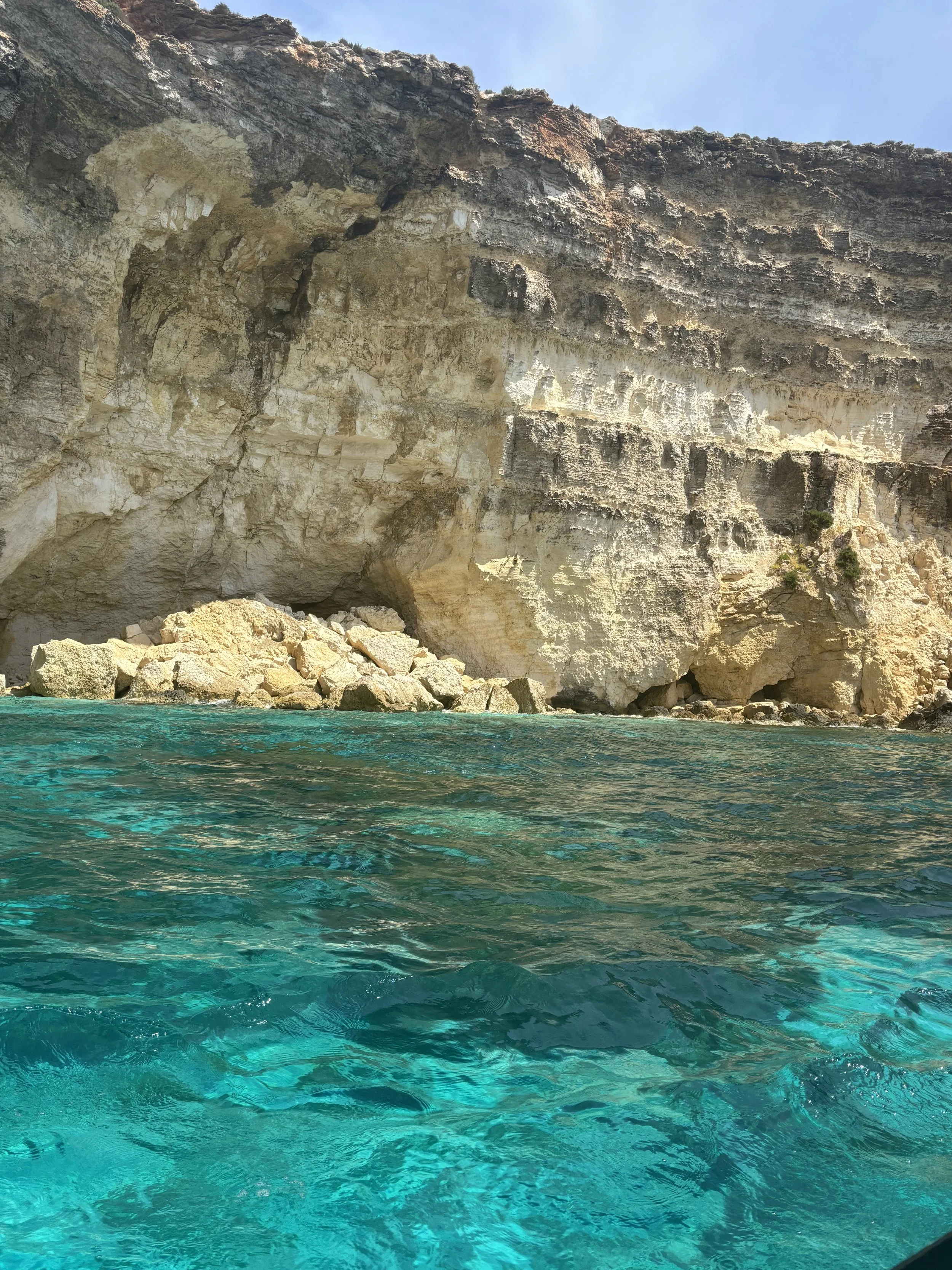 Clear turquoise water with large rocks and a tall, rugged cliff face in the background.