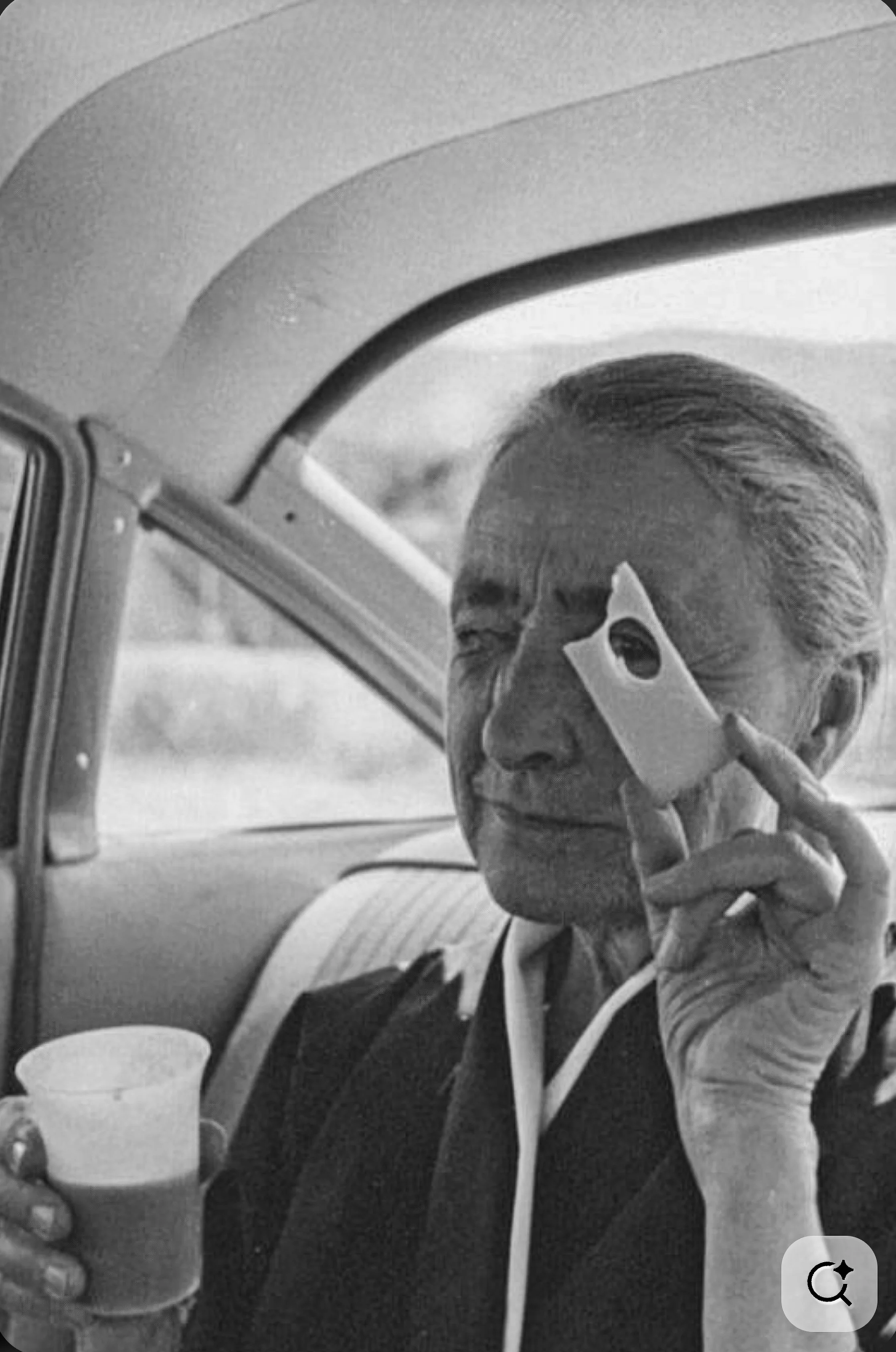 A candid photo of Georgia O'Keeffe in a lighter moment, taken by Tony Vacarro. O'Keeffe sits in the back seat of a car and peers through a hole in a piece of cheese at the photographer