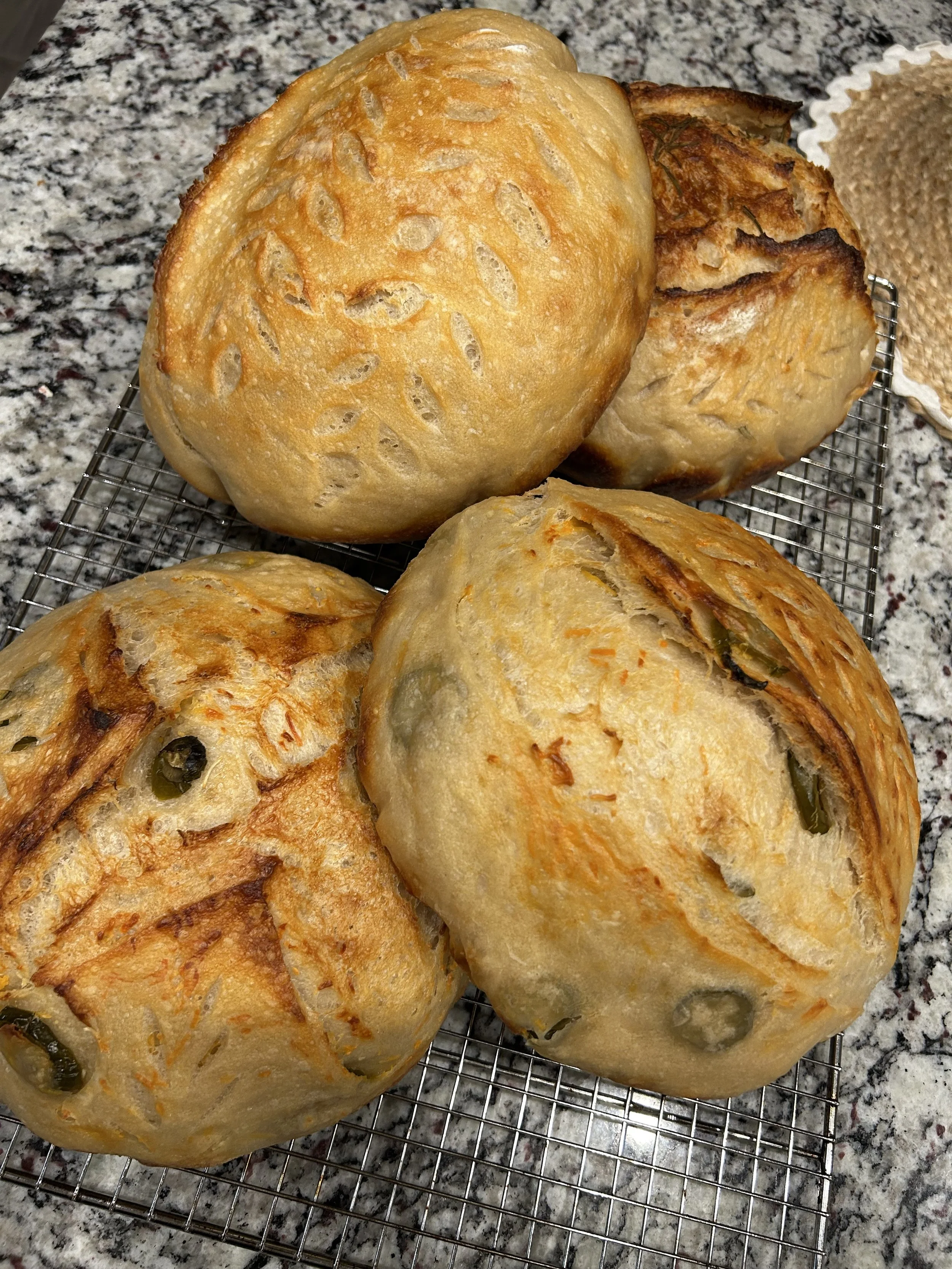 Four baked bread rolls with a golden crust cooling on a wire rack on a speckled granite countertop.