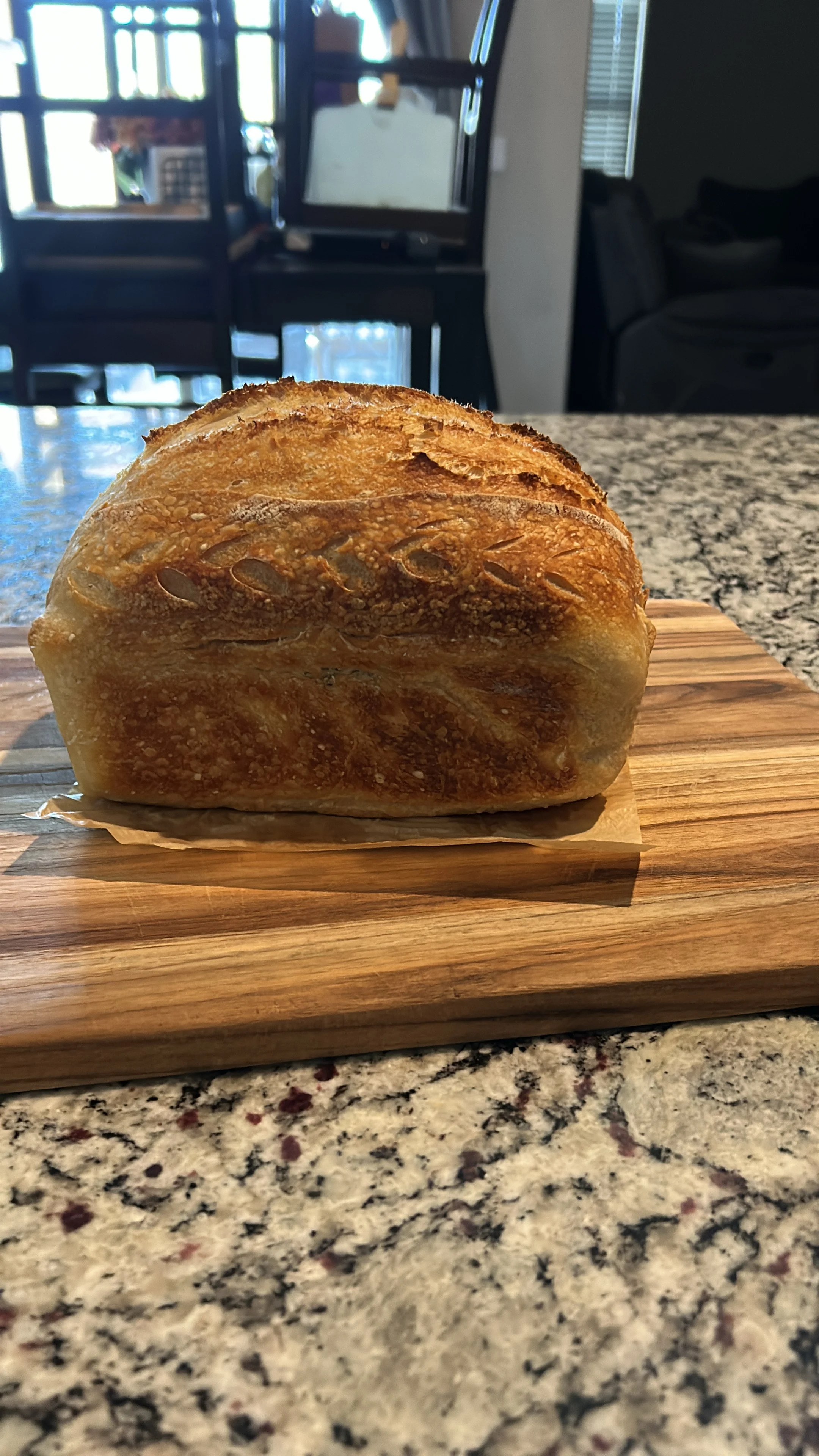 A loaf of freshly baked bread on a wooden cutting board in a kitchen.