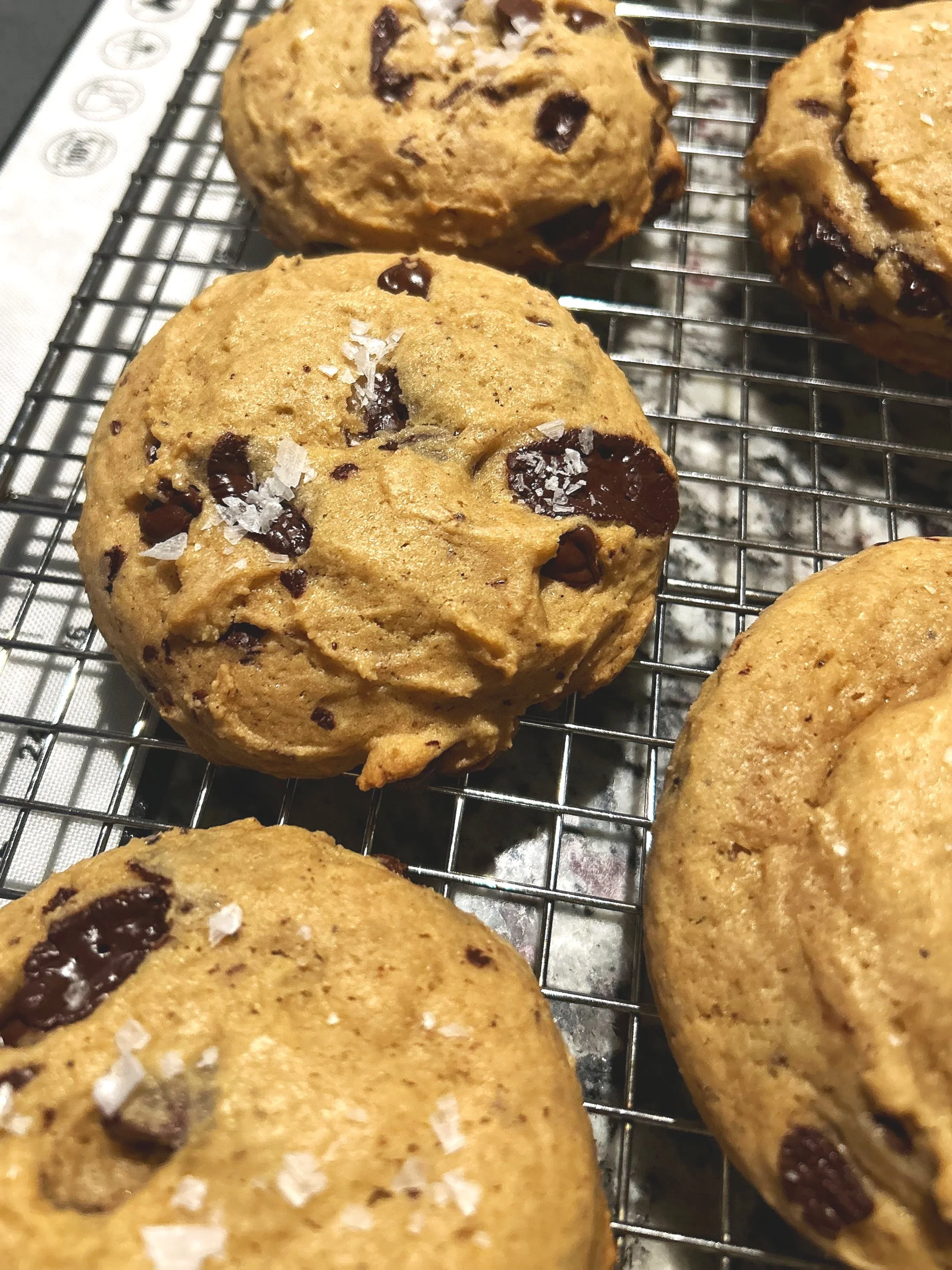 Close-up of freshly baked chocolate chip cookies on a cooling rack, some sprinkled with sea salt.