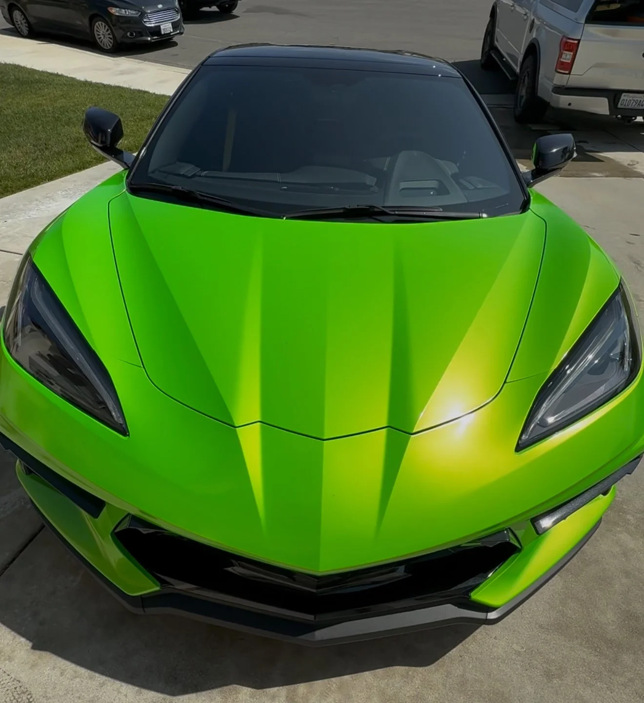 A bright green sports car parked on a driveway, with other vehicles visible in the background.