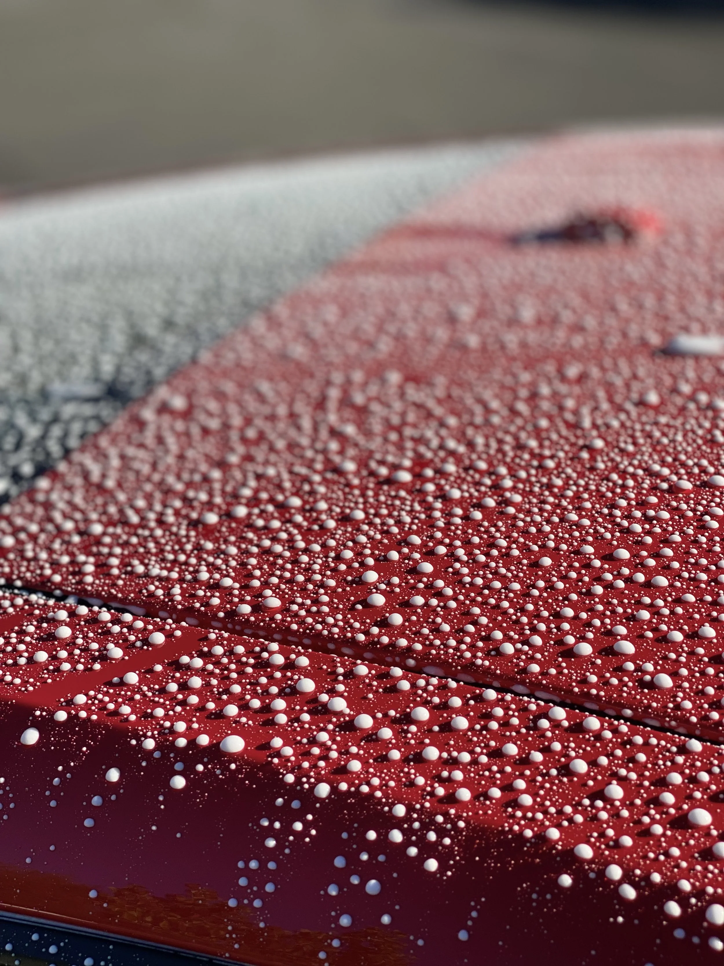 Close-up of a red car's hood covered in water droplets.