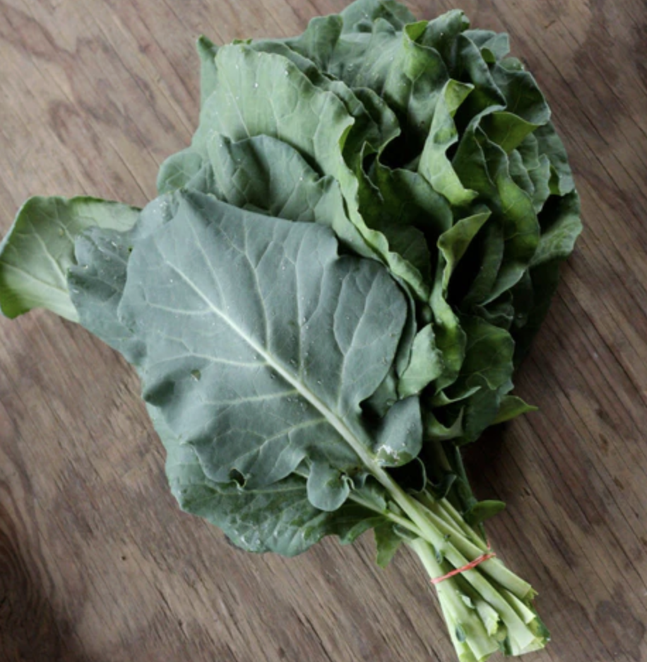 A bunch of fresh green leafy vegetables, likely collard greens or kale, on a wooden surface.