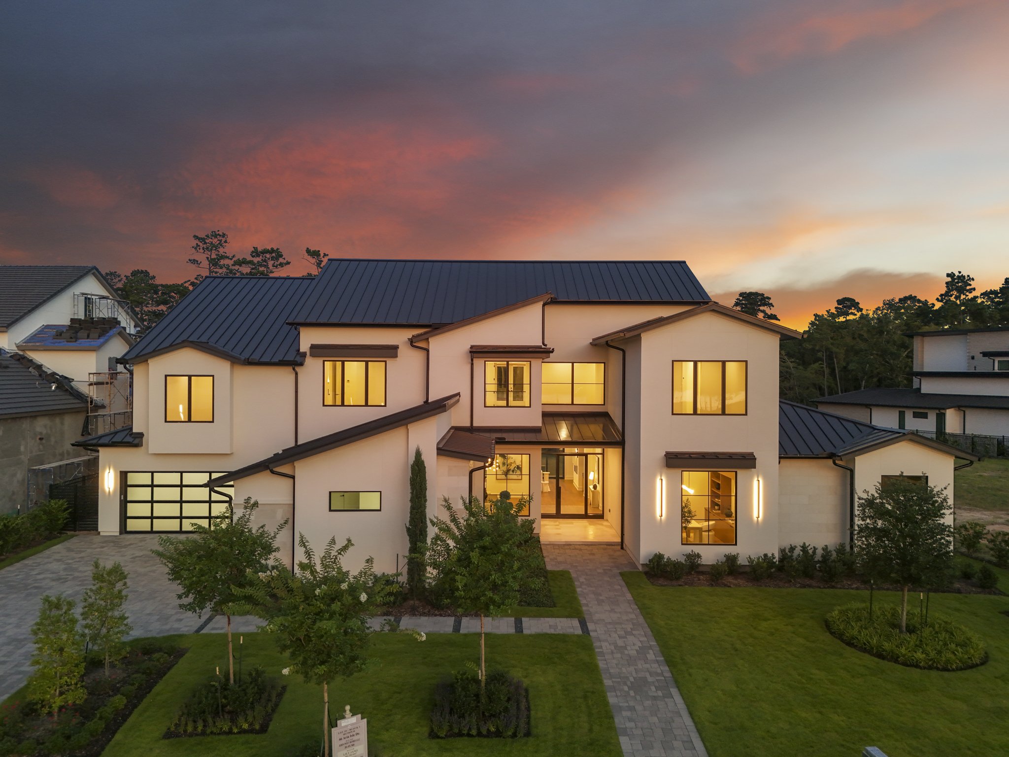 Modern two-story white house with black accents, large windows, and a well-manicured lawn at dusk.