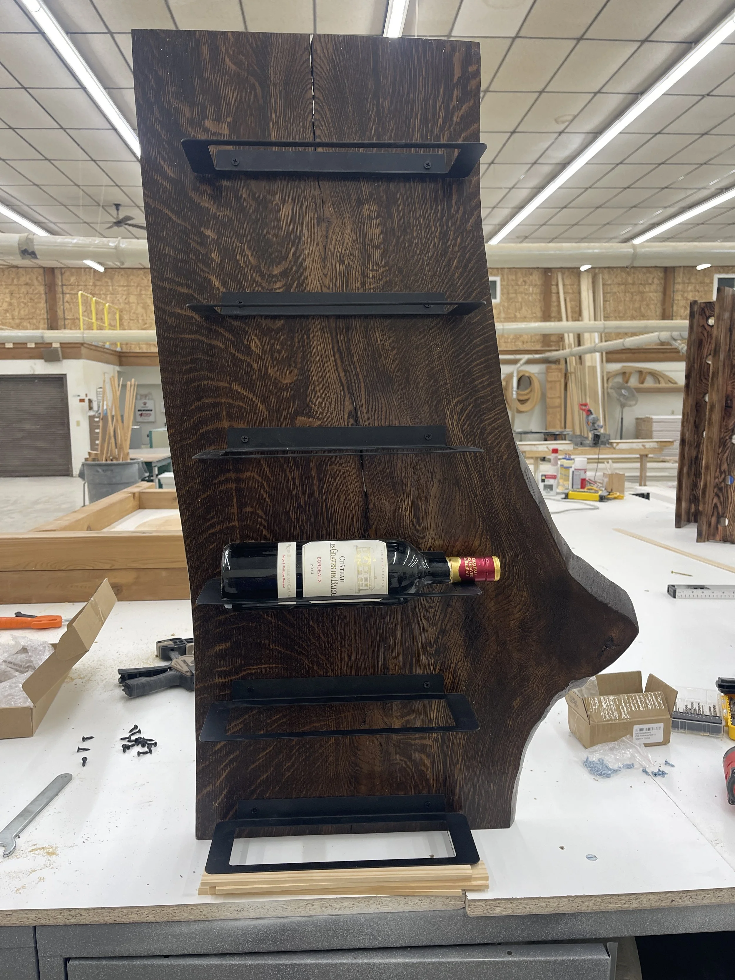 Side view of a wooden wine rack with a bottle of red wine in one of the slots, set in a woodworking shop.