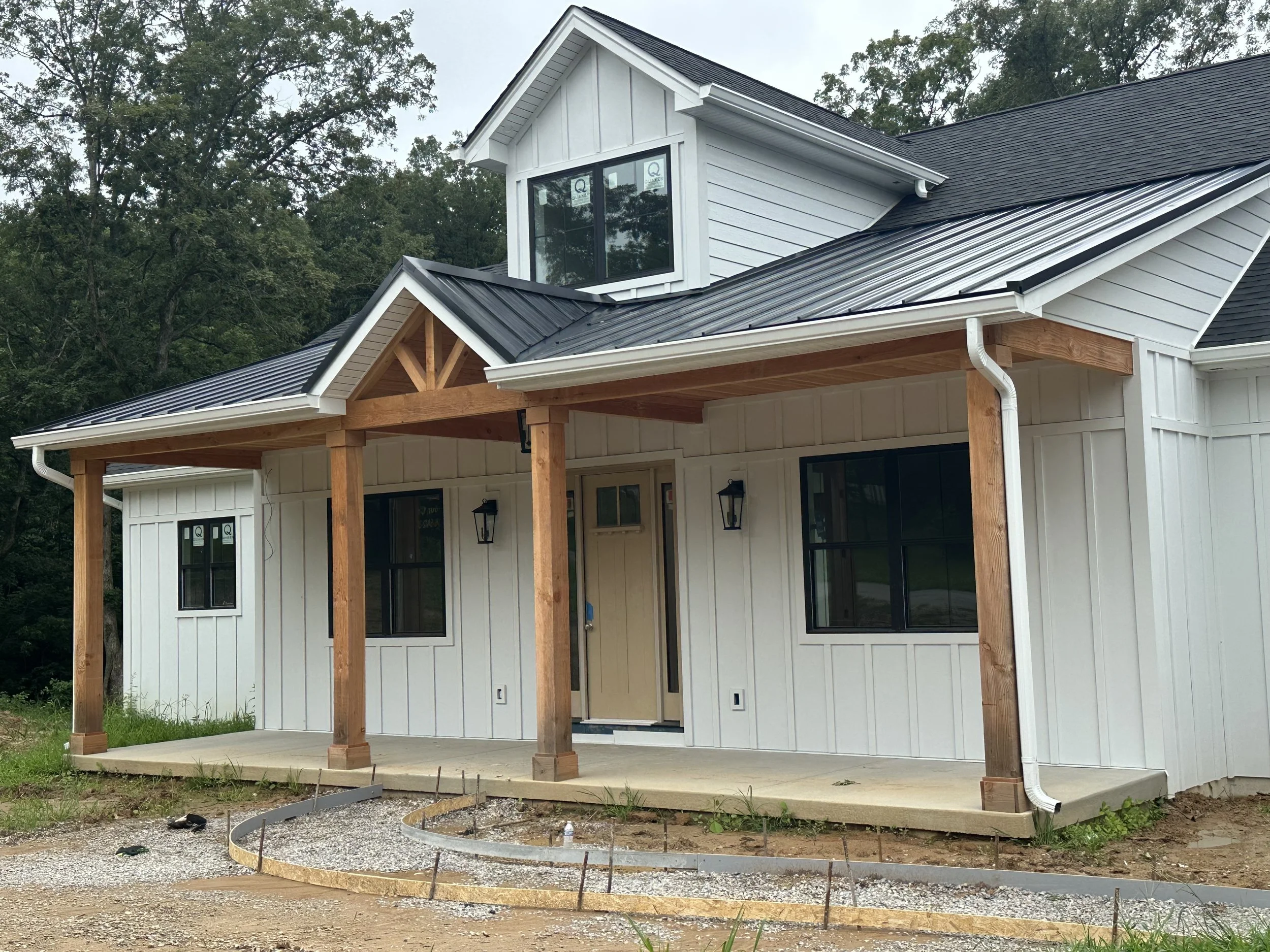 New house under construction with white siding, black roof, and wooden porch pillars.