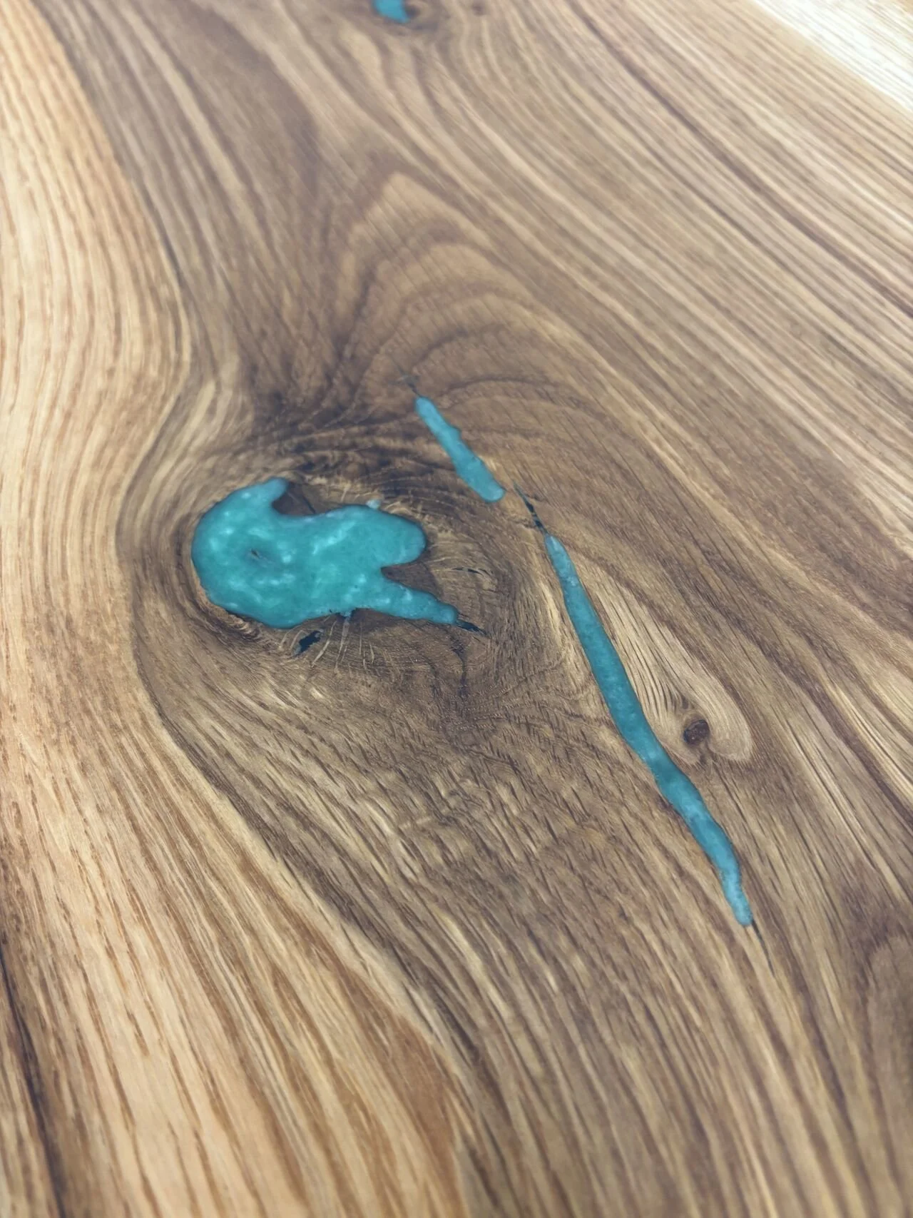 Close-up of a natural wood surface with a knot and two streaks of blue resin or paint.