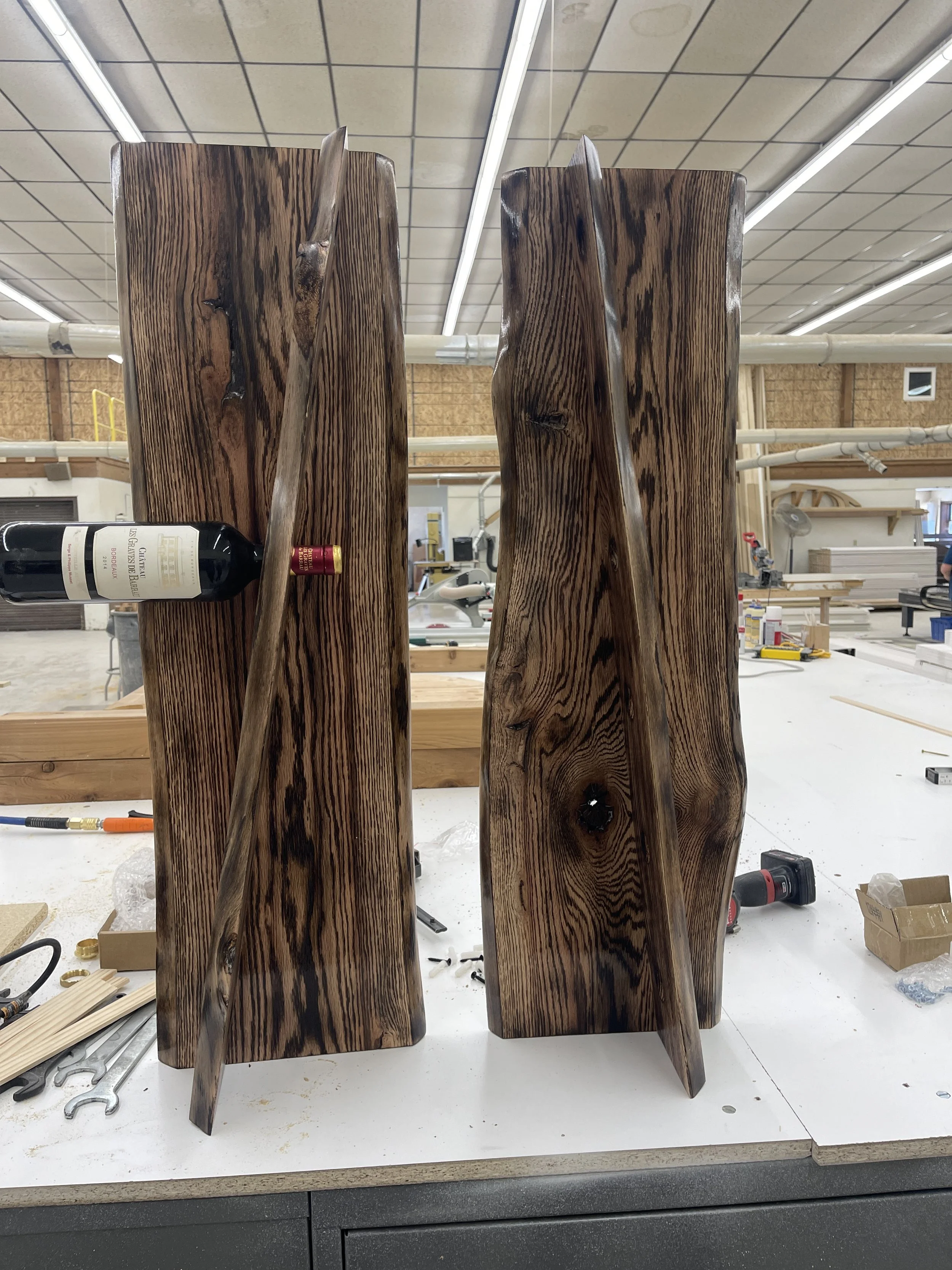 Two large, polished wooden sculptures with a dark finish and organic shapes, placed on a workbench in a woodworking shop.