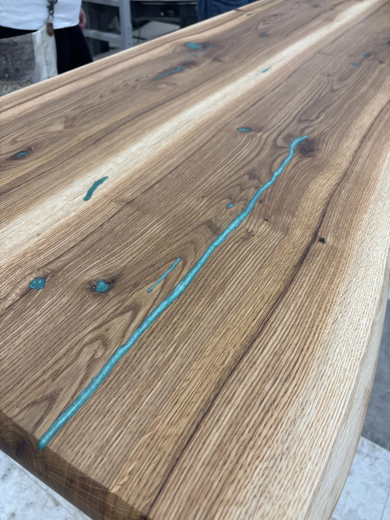 Close-up of a wooden tabletop with blue resin inlay accent along the grain and knots in the wood.
