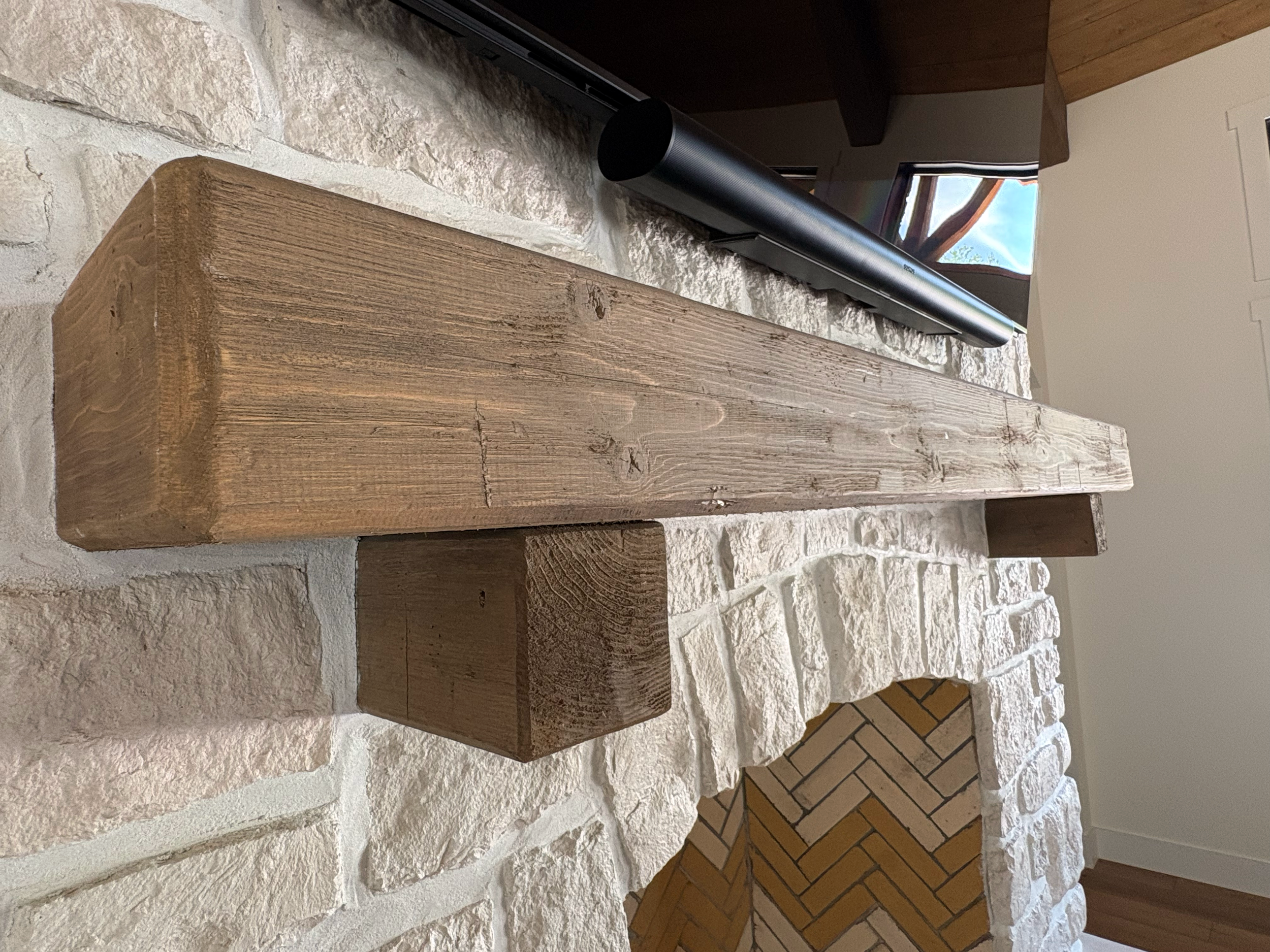 Close-up view of a wooden mantlepiece above a white painted stone fireplace with a black soundbar below.