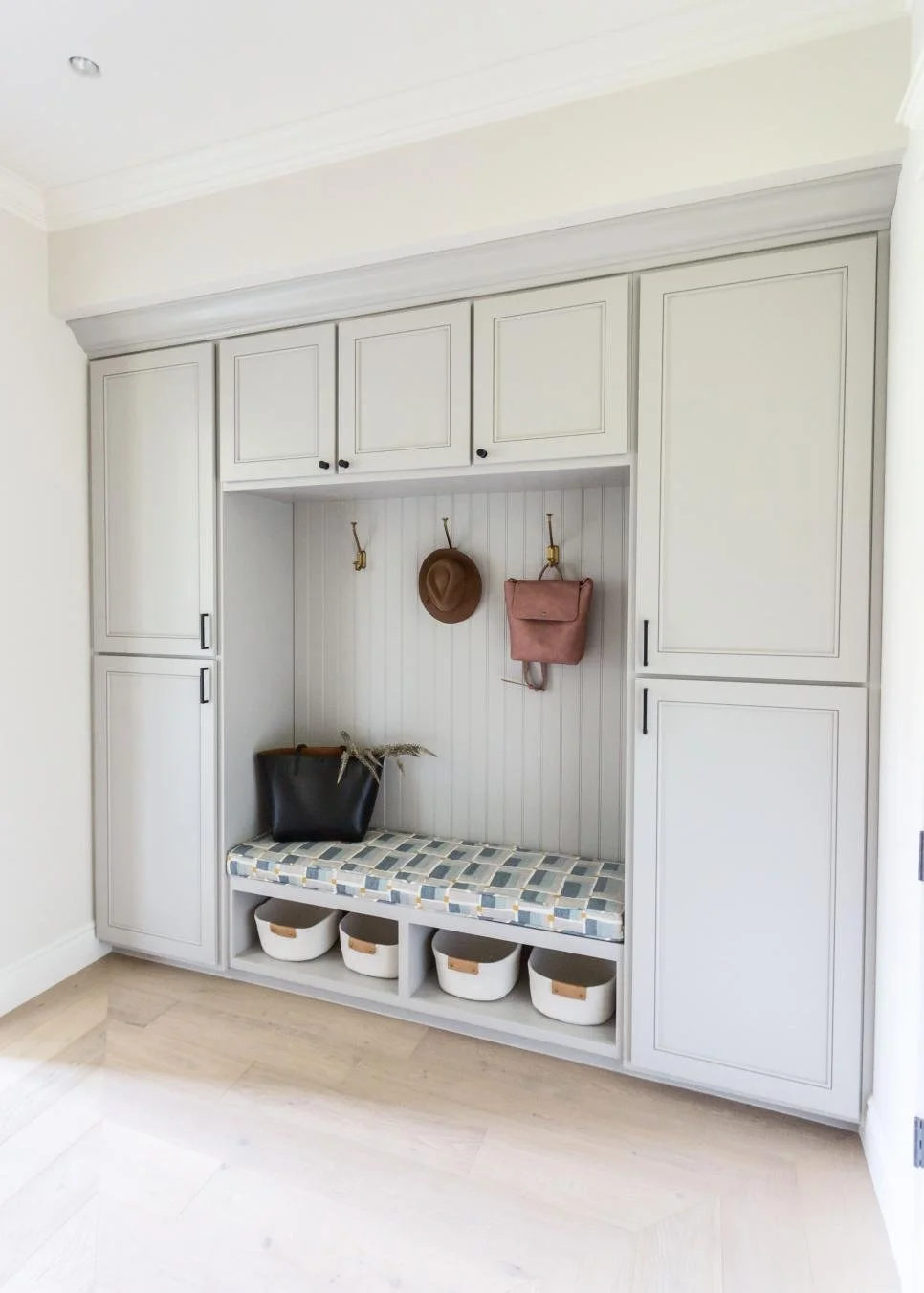 Built-in mudroom storage unit with cabinets, hooks, a bench with storage underneath, and accessories including a hat, purse, and bags.