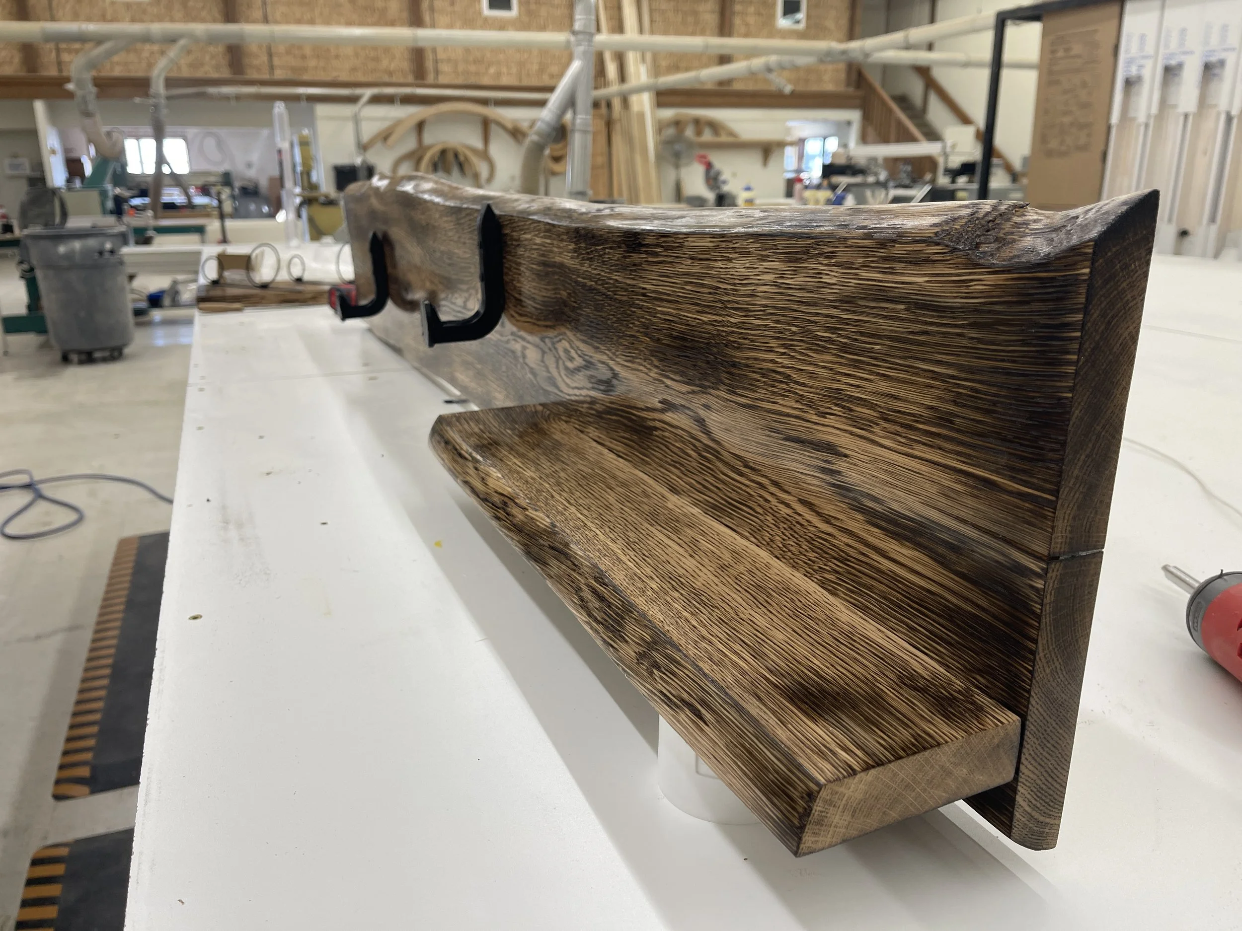 A wooden shelf being crafted in a woodworking shop, with clamps holding it in place and tools scattered in the background.