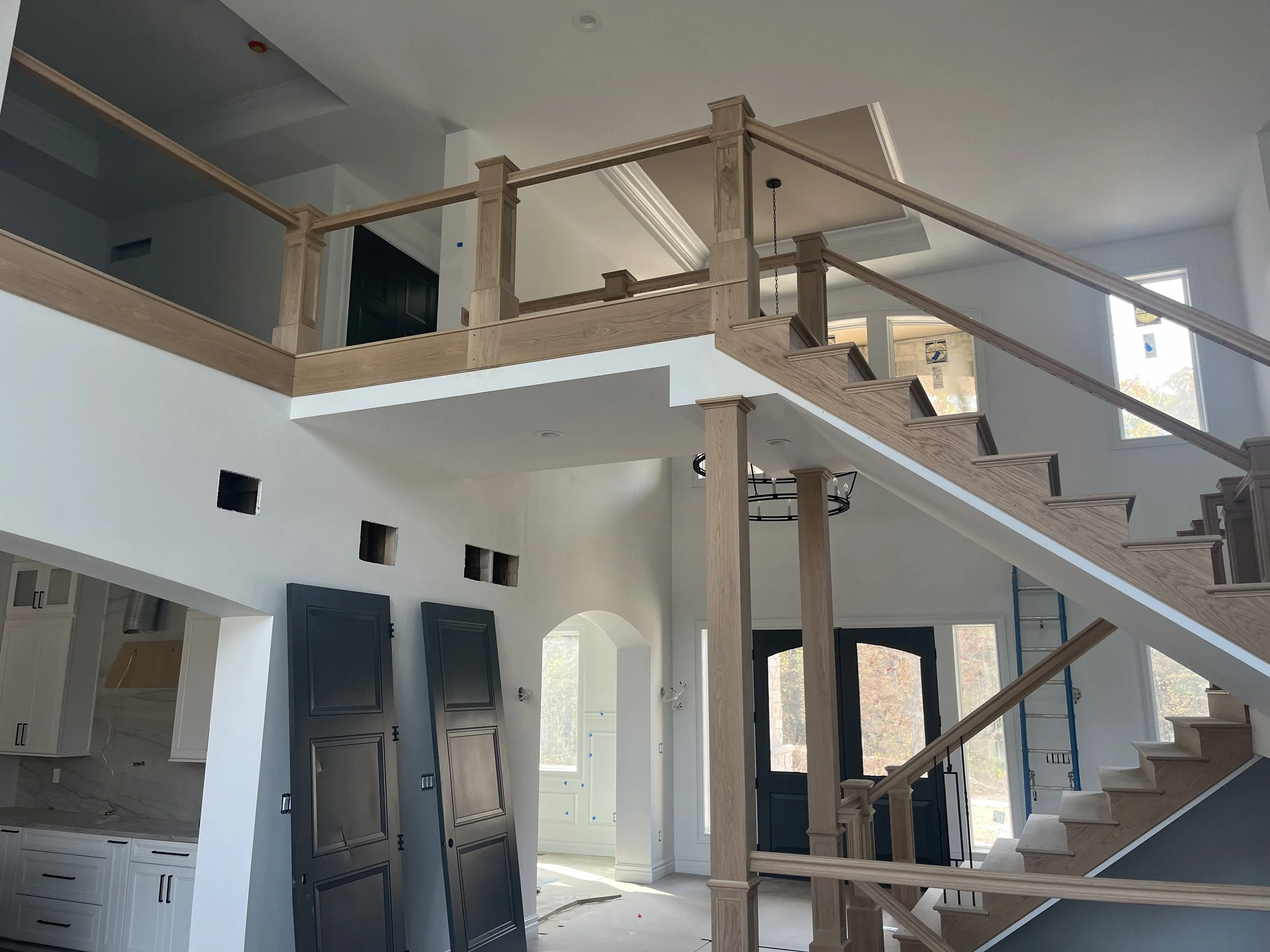 Interior of a house under construction with wooden staircase, white walls, and windowed doors.