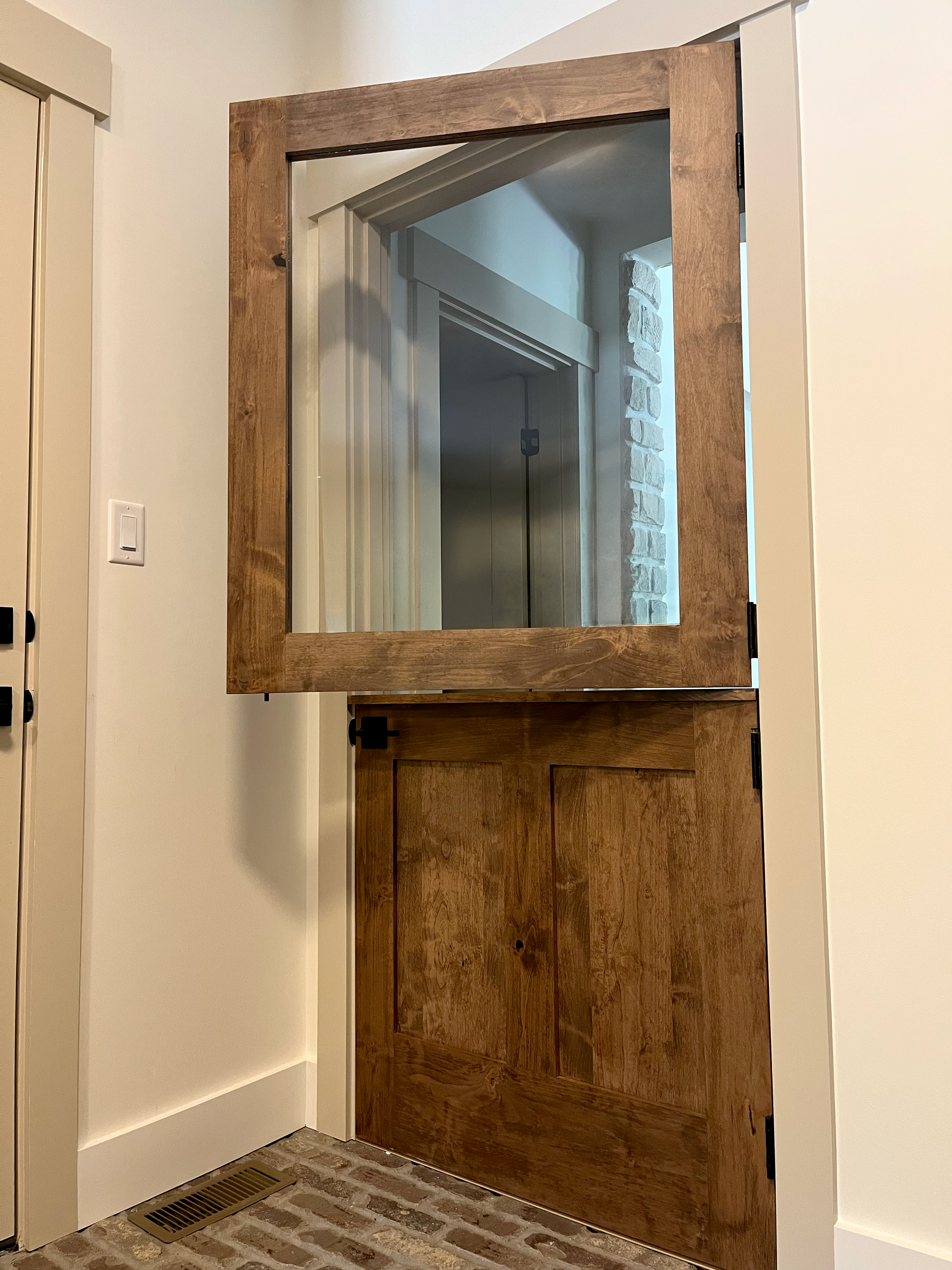 Interior view of a doorway with a large mirror framed with wood, reflecting an elevator and brick wall inside a building, and a white wall on the right side.