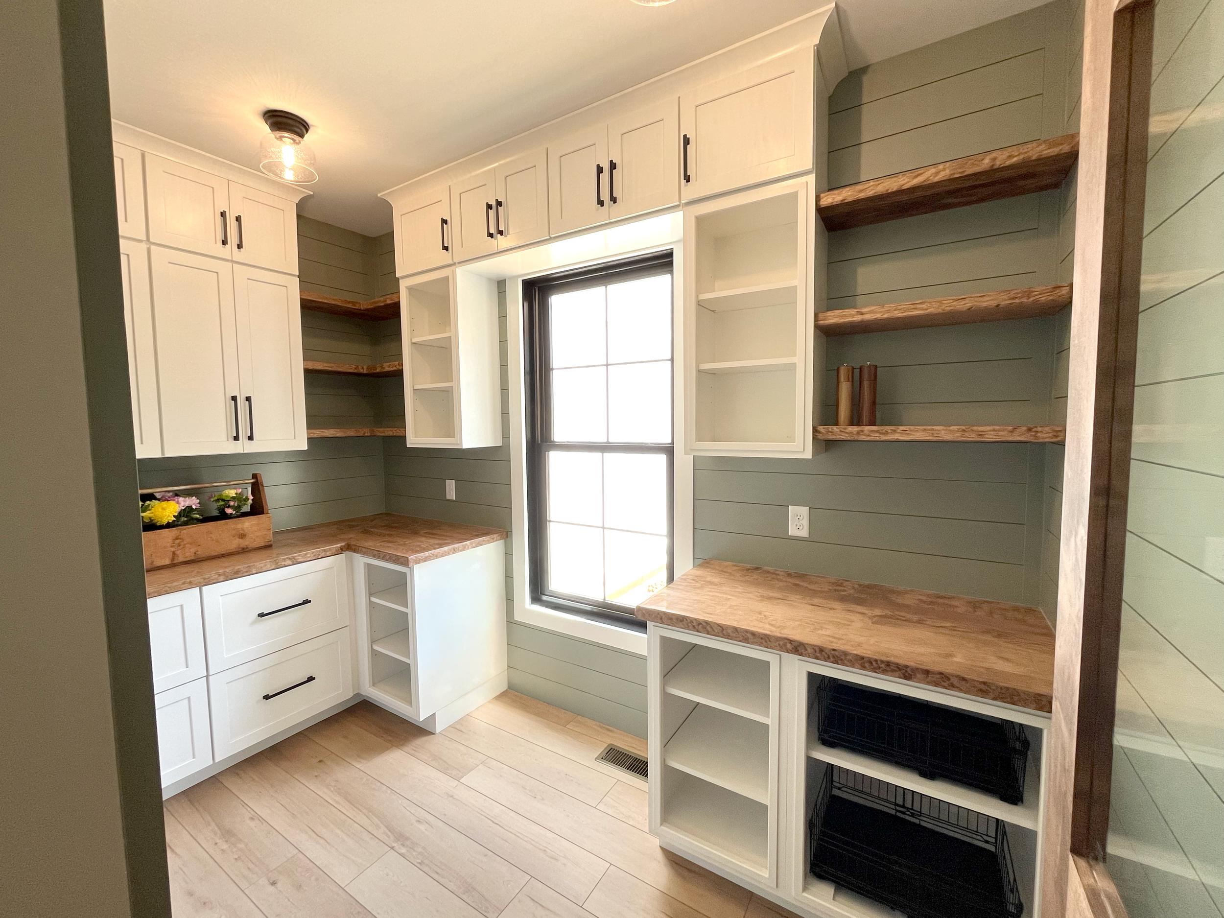 Kitchen with white cabinets, wooden shelves, a window, and a flower box on the countertop.