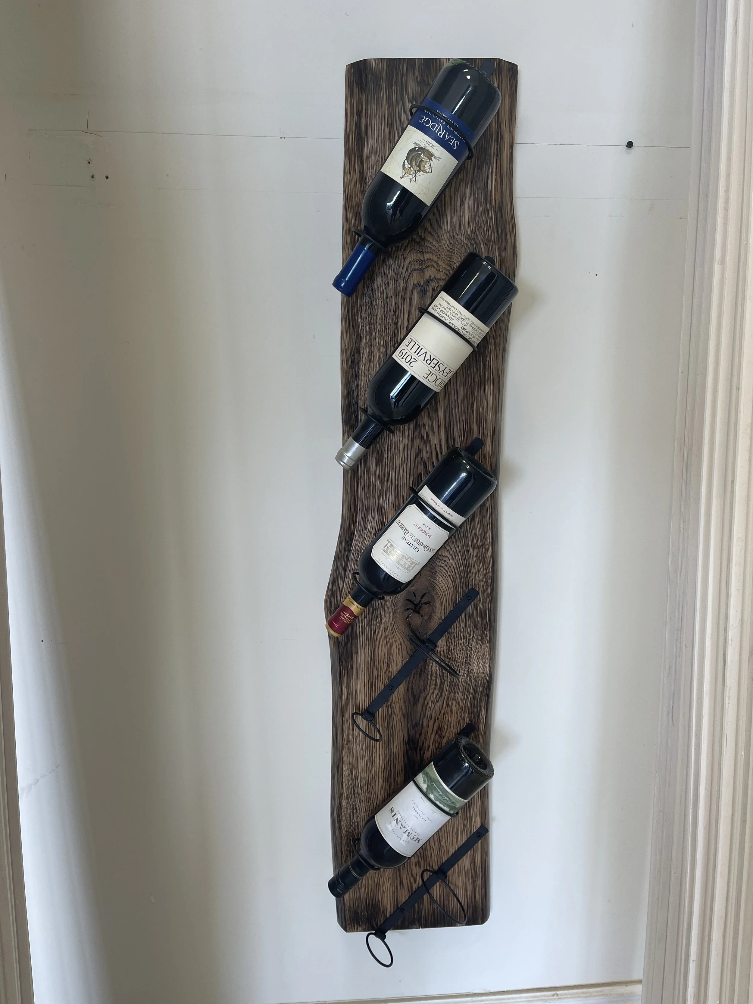 A wooden wall rack holding five bottles of wine and two corkscrews.