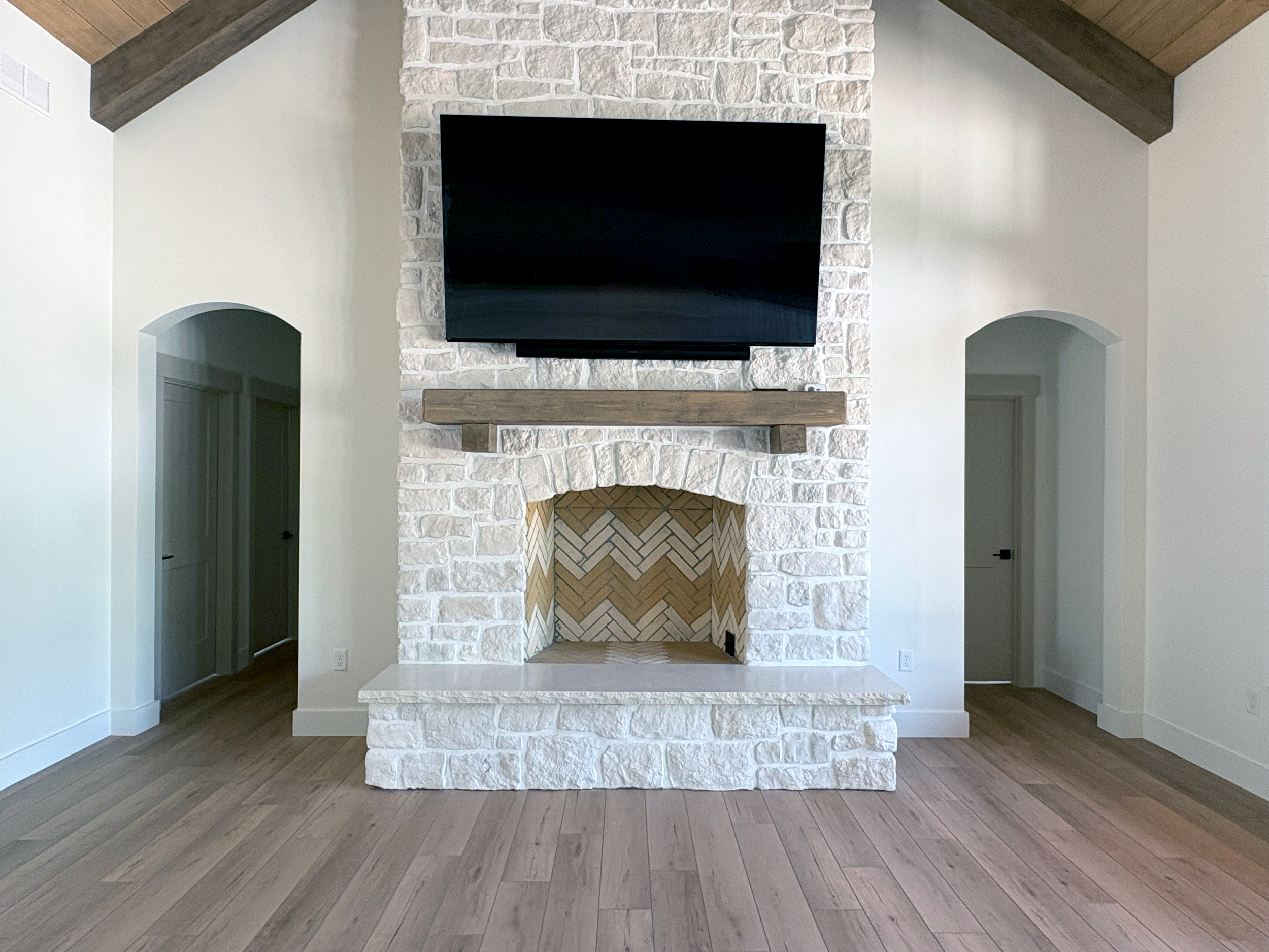 A white brick fireplace with a wooden mantel in a modern living room with hardwood floors and two arched doorways.
