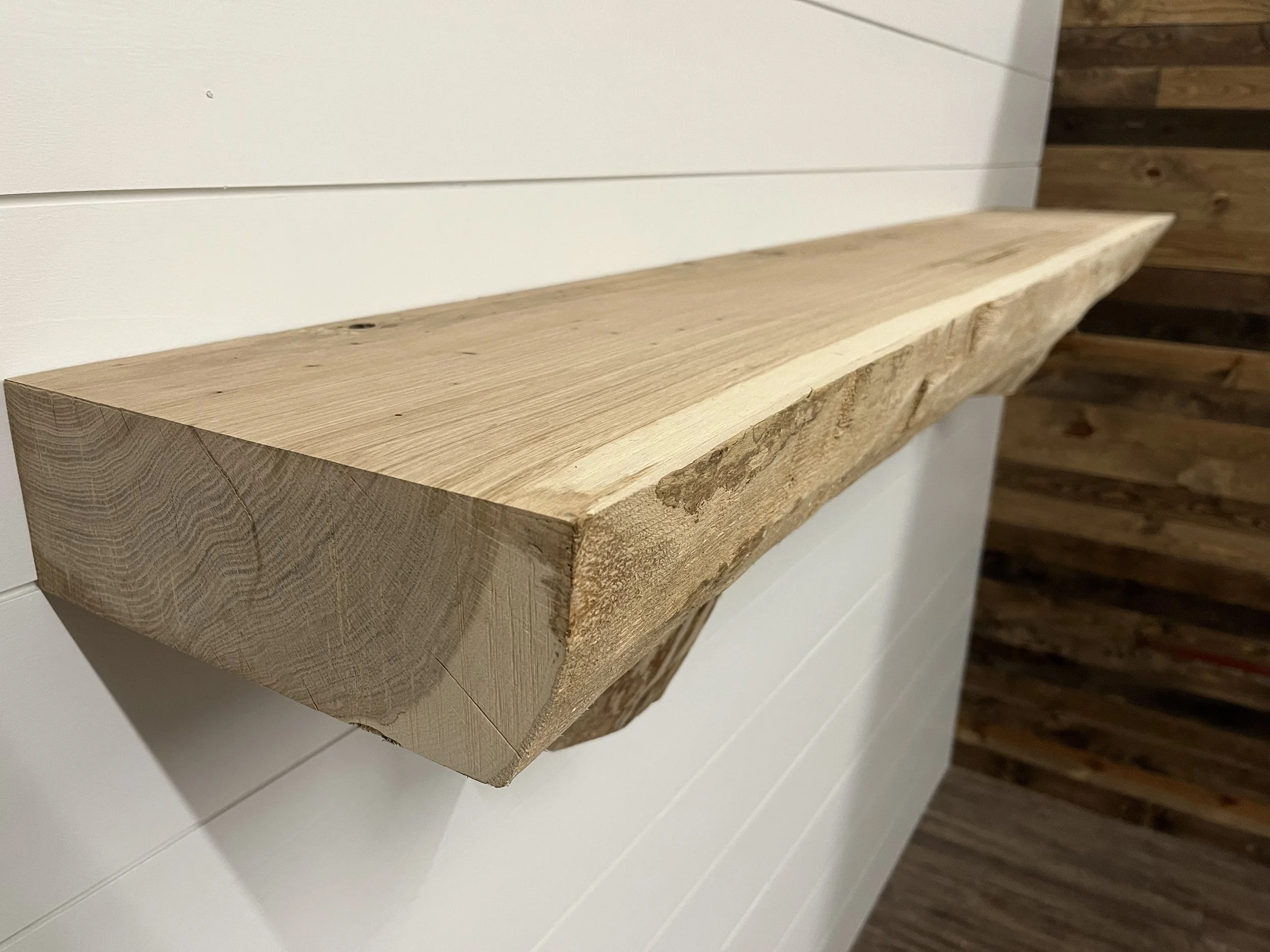 A wooden shelf made from a thick, natural wood slab mounted on a white paneled wall with a wooden accent wall in the background.