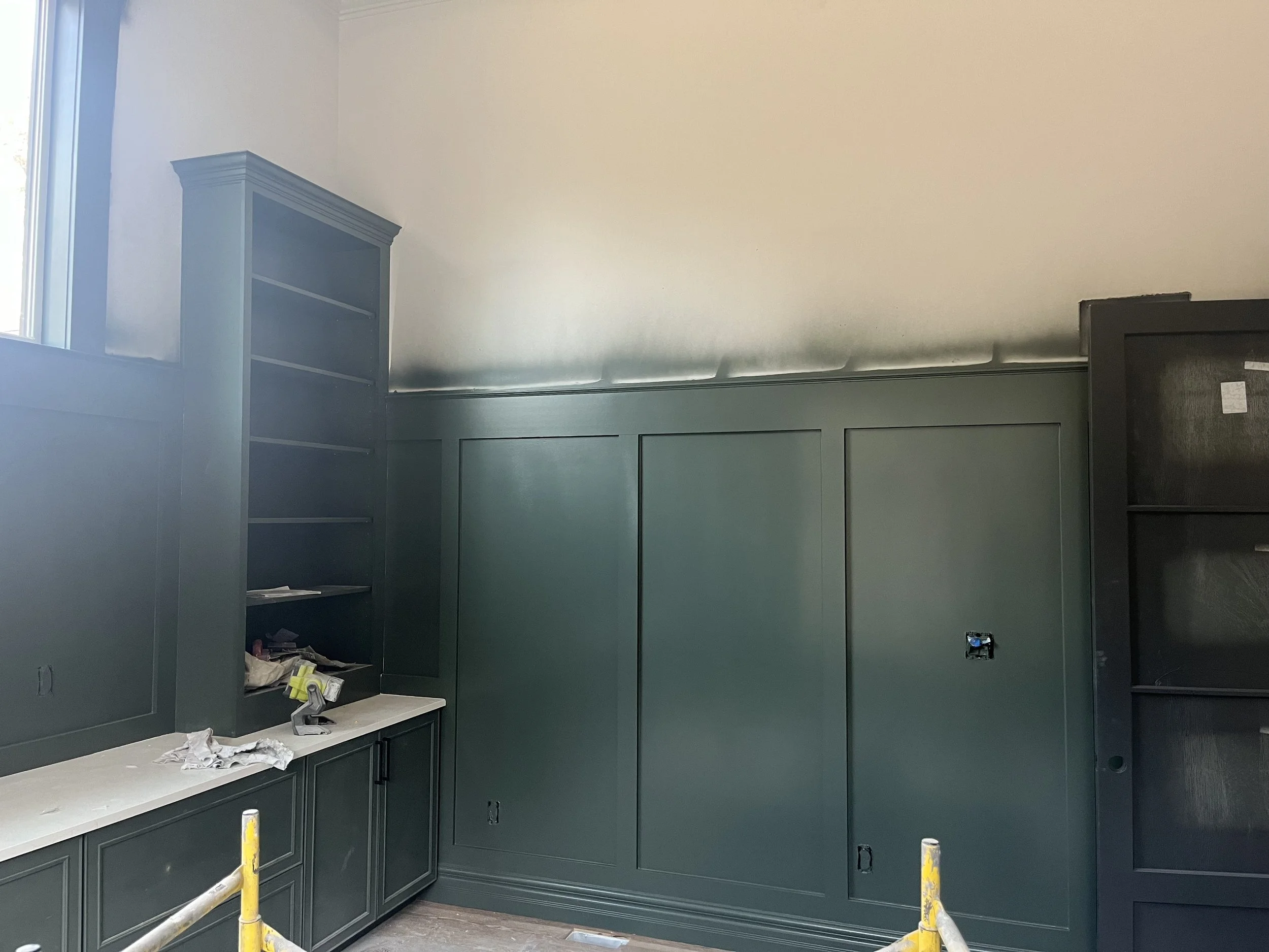 Room under construction with green painted wall paneling, a built-in cabinet with open shelves, and a window on the left side.