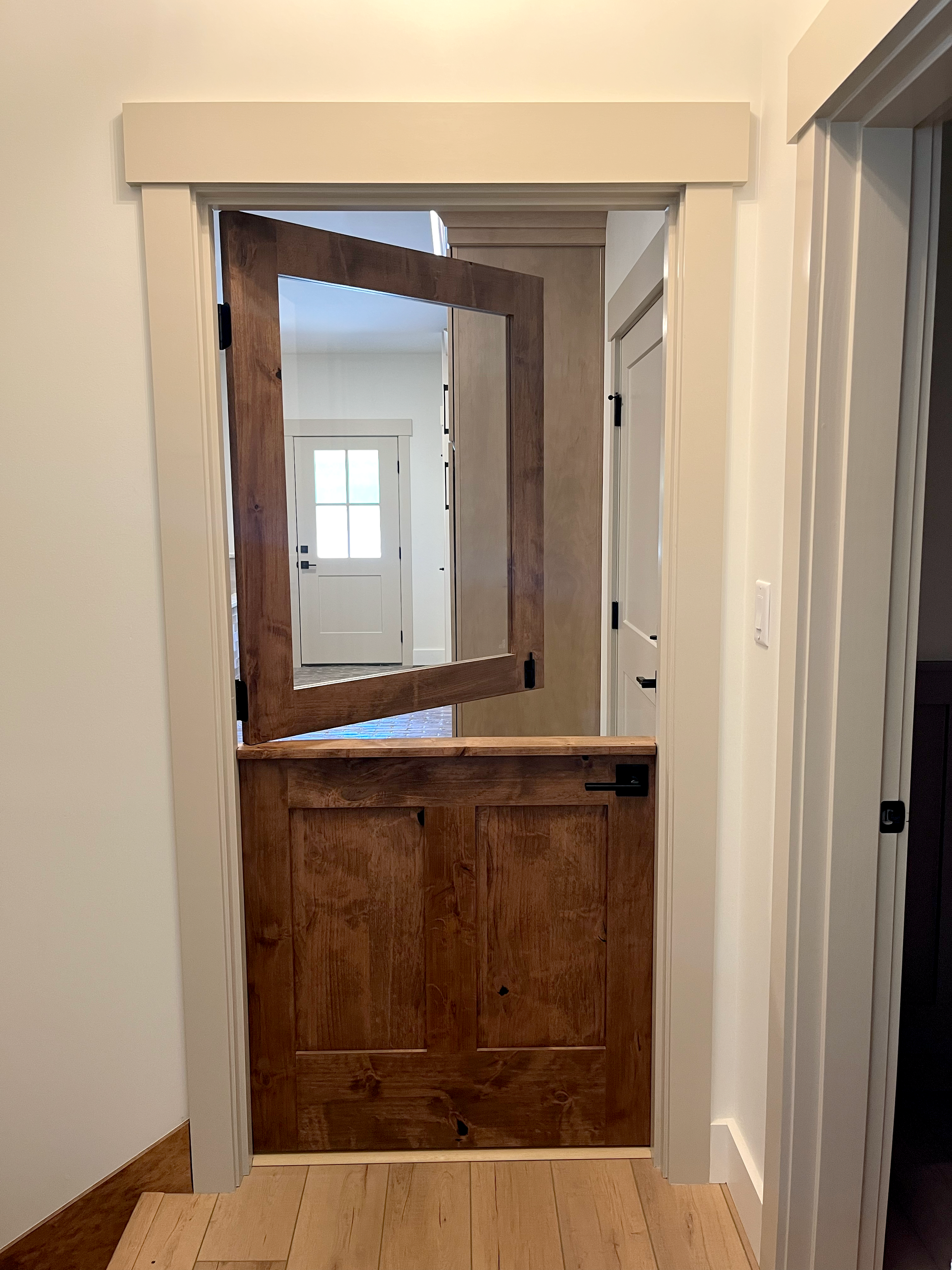 Multiple wooden doors in a doorway with white trim and beige walls. The doors are partially open, revealing additional doors and a window in the background.