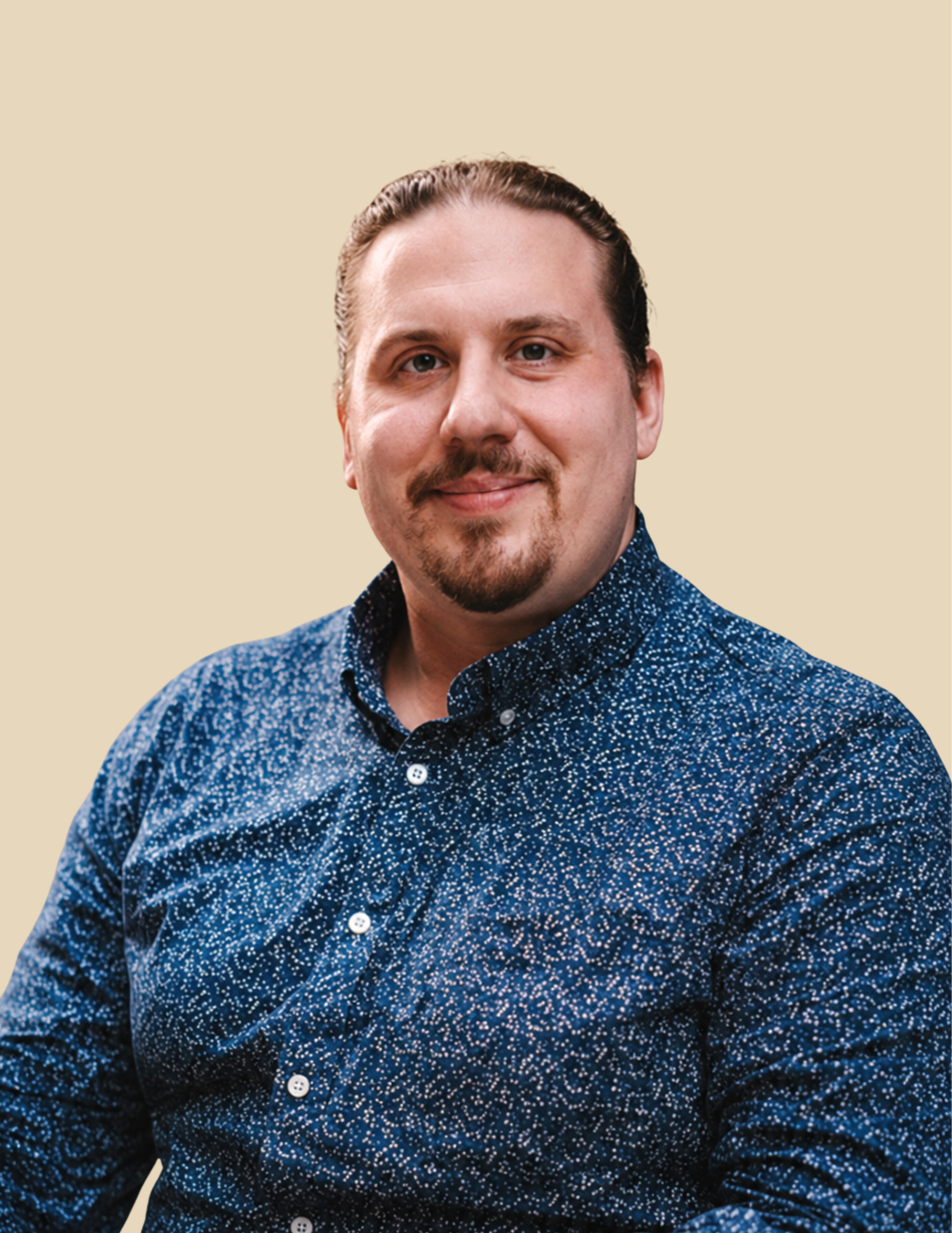 A man with a beard and mustache, wearing a patterned blue button-up shirt, sitting against a plain beige background. Paul Fitzgerald, LCSW. Therapist at ThirdSpace Psychotherapy, New York City. Aetna Student Health, NYU