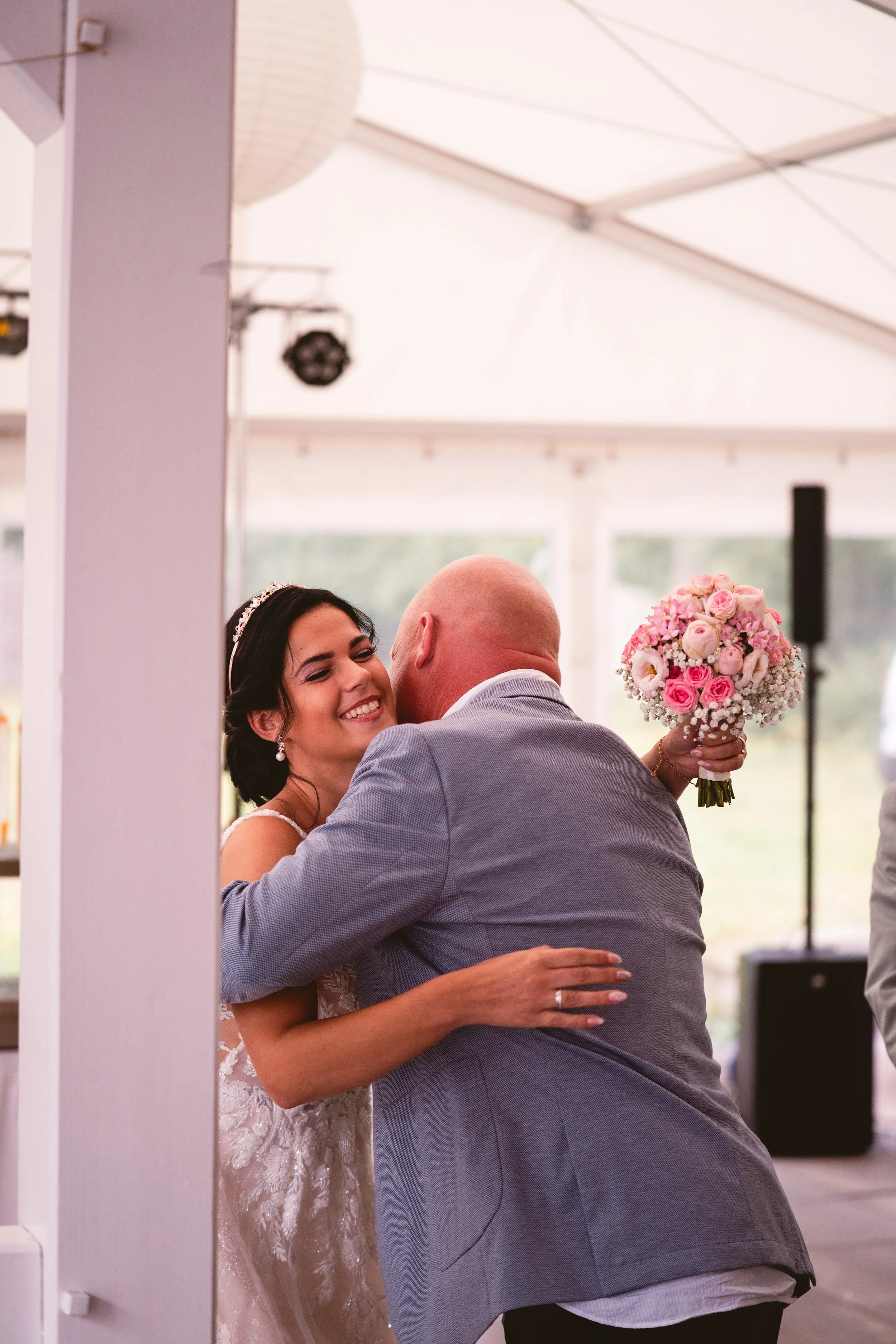Ein Brautpaar bei einem Tanz, die Braut lächelt glücklich, trägt ein weißes Hochzeitskleid mit Spitzen, der Bräutigam trägt einen grauen Anzug.