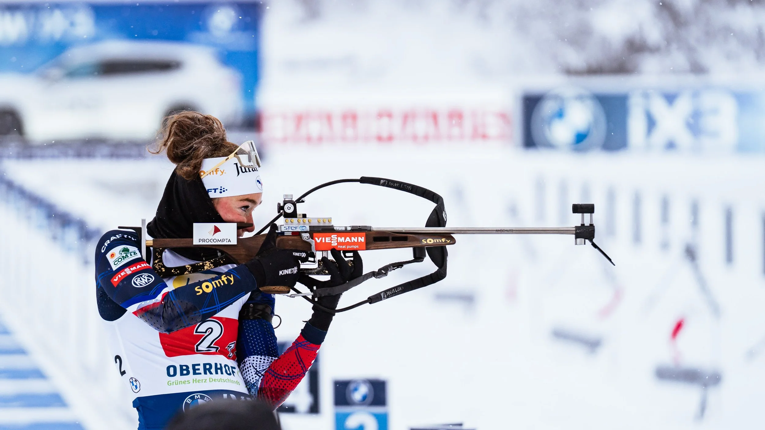 Eine Skifahrerin beim Biathlon zielt mit einem Gewehr auf einen Zielbereich im Wintersportstadion bei kältem Wetter.