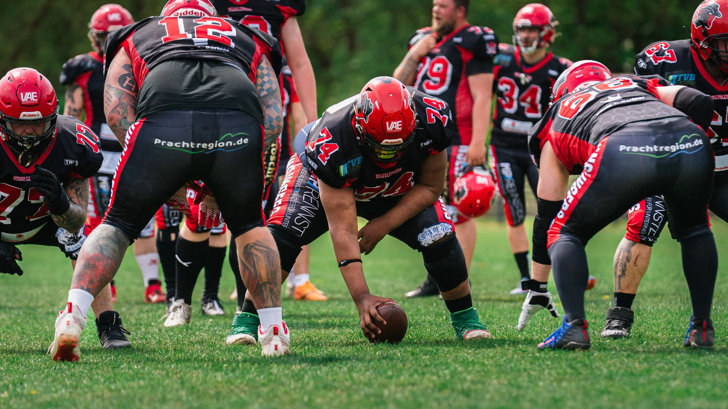 Amerikanischer Footballspieler in Position, bereit den Football zu snappen, umgeben von Teamkollegen auf dem Spielfeld.