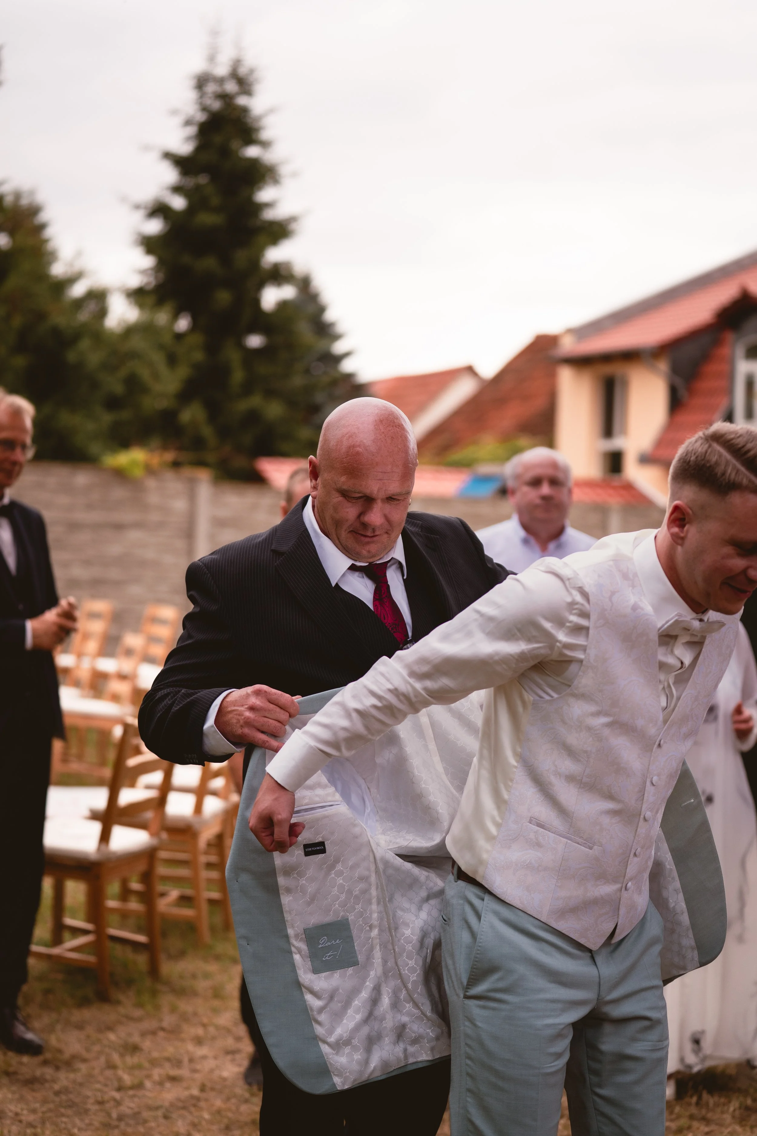 Männer bei einer Hochzeit, die sich an den Händen im Kreis halten, im Freien, während die Braut ihren Schleier trägt.