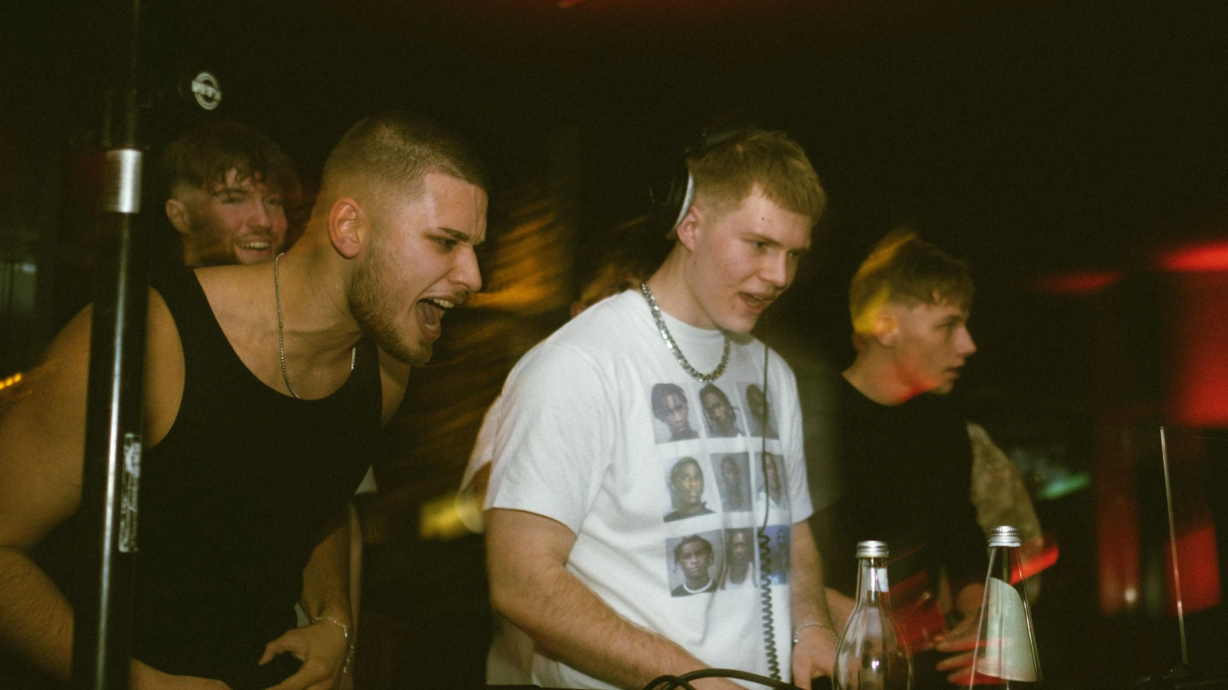 Vier junge Männer beim DJ-Auflegen in einem Club, mit dunklem Hintergrund und gedämpfter Beleuchtung.