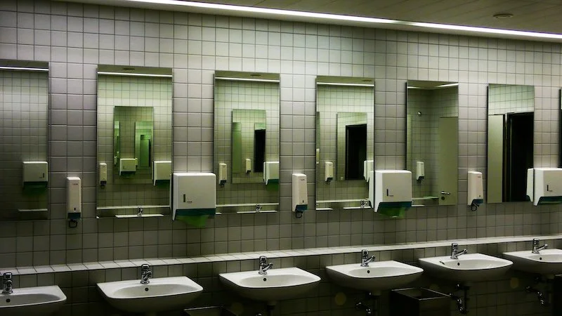 A row of sinks with mirrors and soap dispensers in a public restroom.