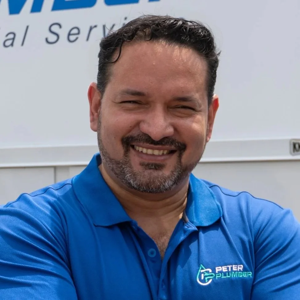 A man smiling wearing a blue polo shirt with a company logo that says "Peter Plumber," standing in front of a white background with partial text visible.