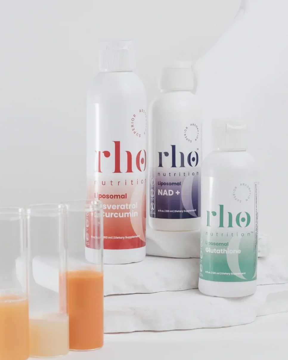 Bottles of dietary supplements labeled 'r|ho' with different formulations, including Liposomal NAD+ and Glutathione, alongside small test tubes filled with colorful liquids.