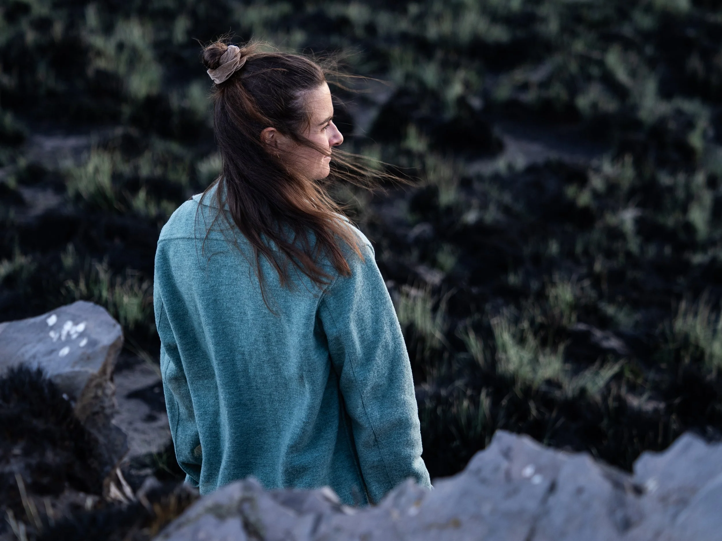 Junge Frau mit braunen Haaren in türmeligem Raum, die nach rechts blickt, vor einer dunklen, bewachsenen Landschaft.
